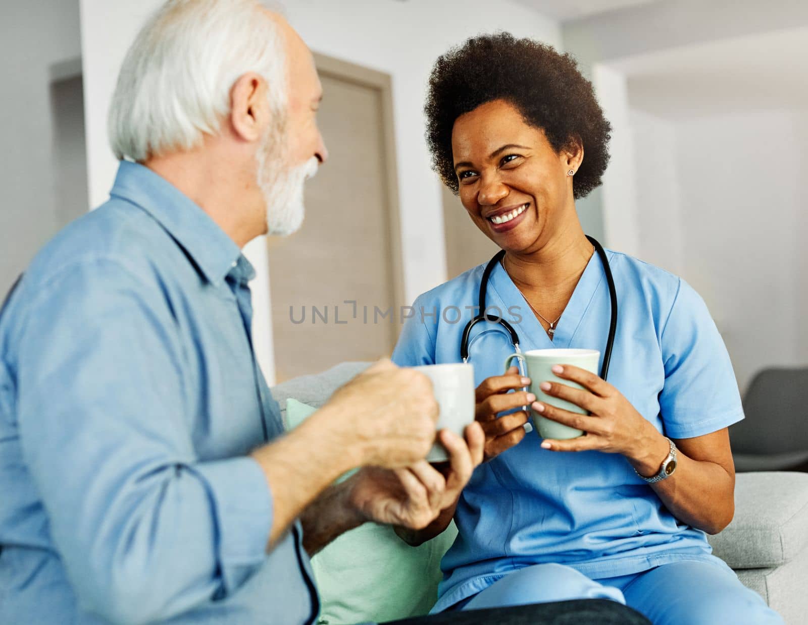 Doctor or nurse caregiver with senior man drinking tea or coffee at home or nursing home