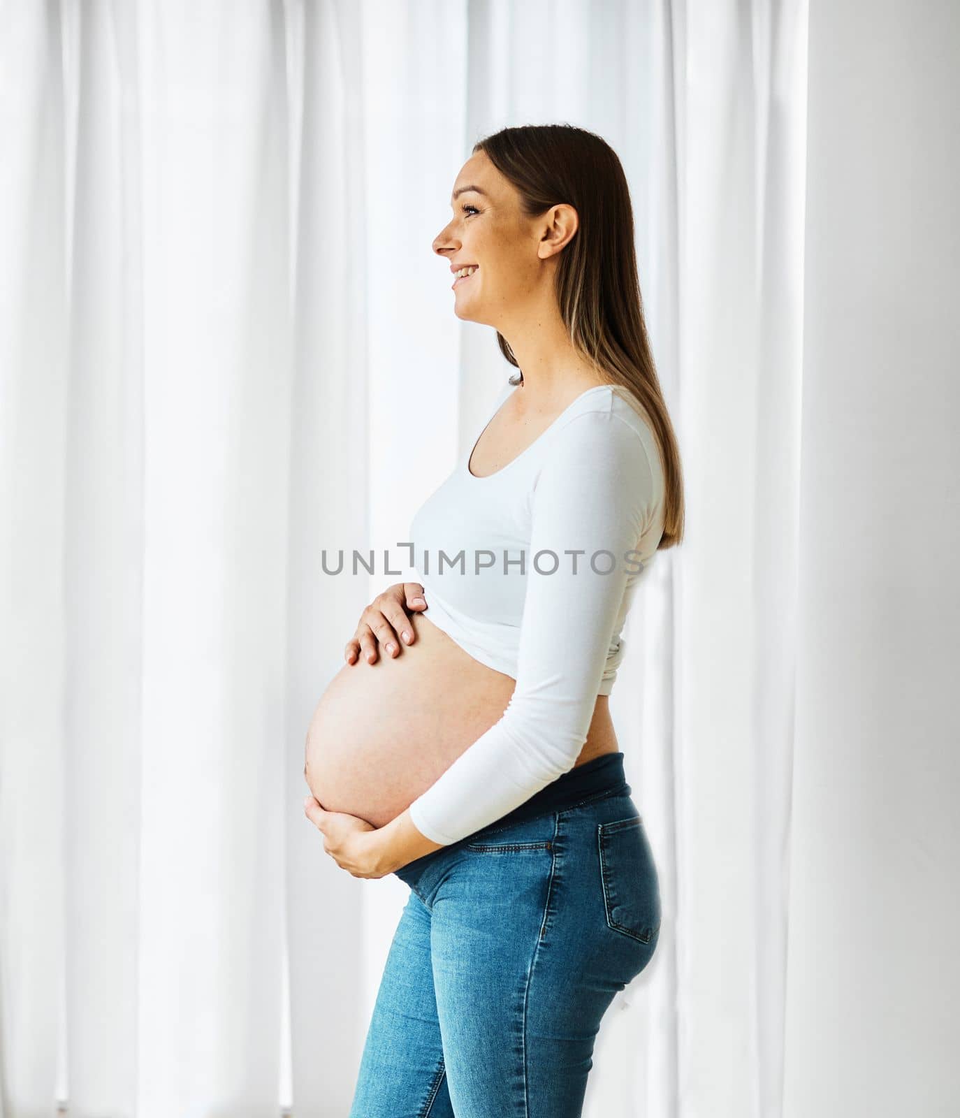 Portrait of a happy young pregnant woman holding her belly at home