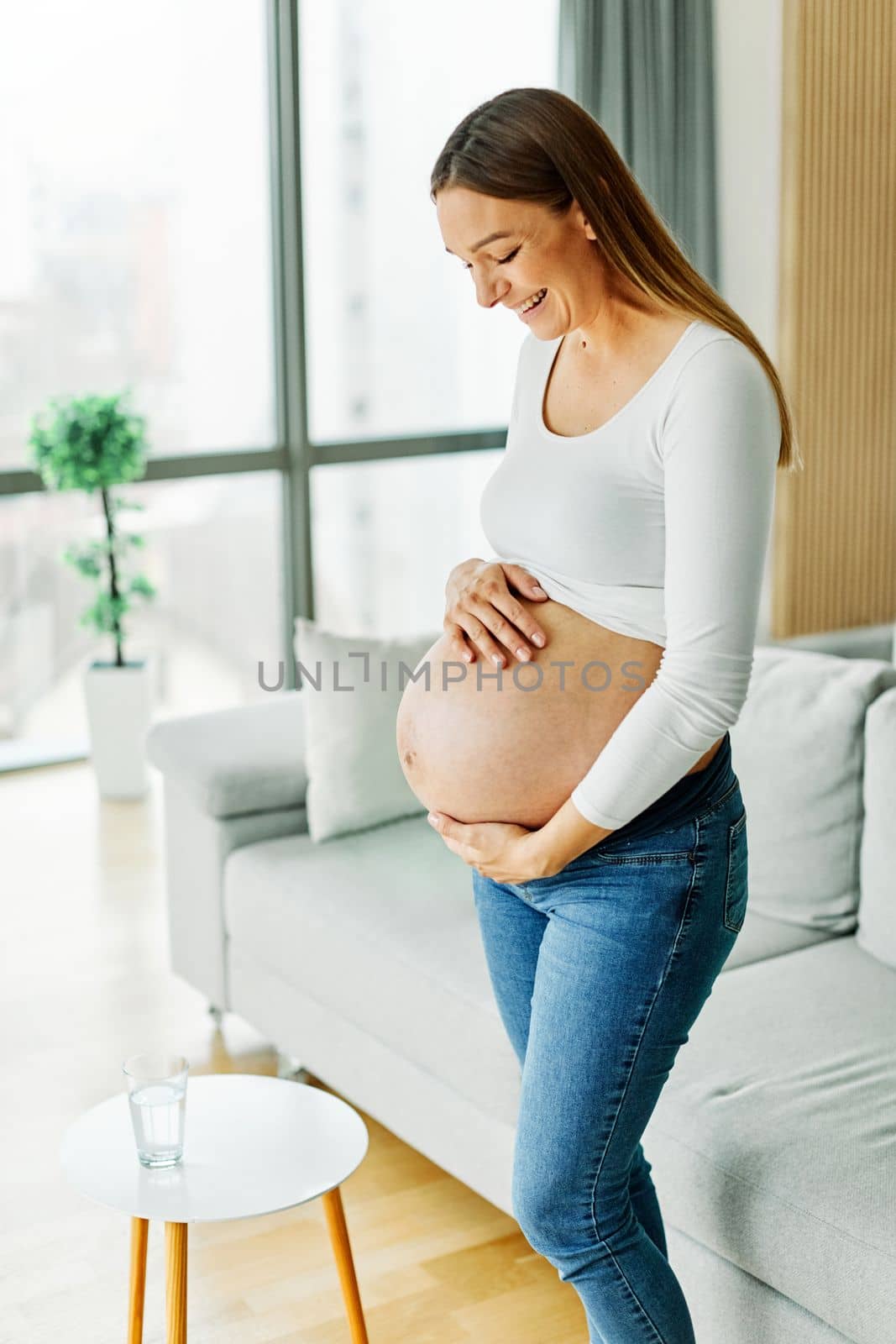 Portrait of a happy young pregnant woman holding her belly at home