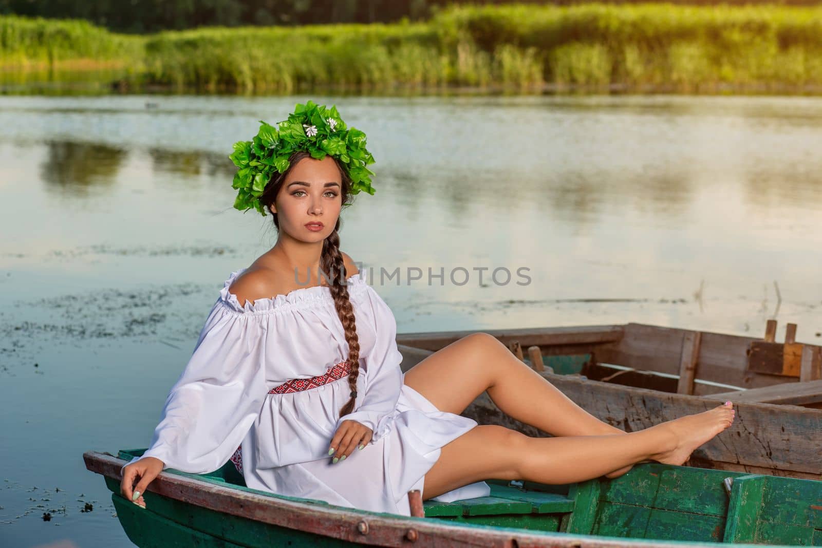 Young sexy woman on boat at sunset. The girl has a flower wreath on her head, relaxing and sailing on river. Fantasy art photography. by nazarovsergey