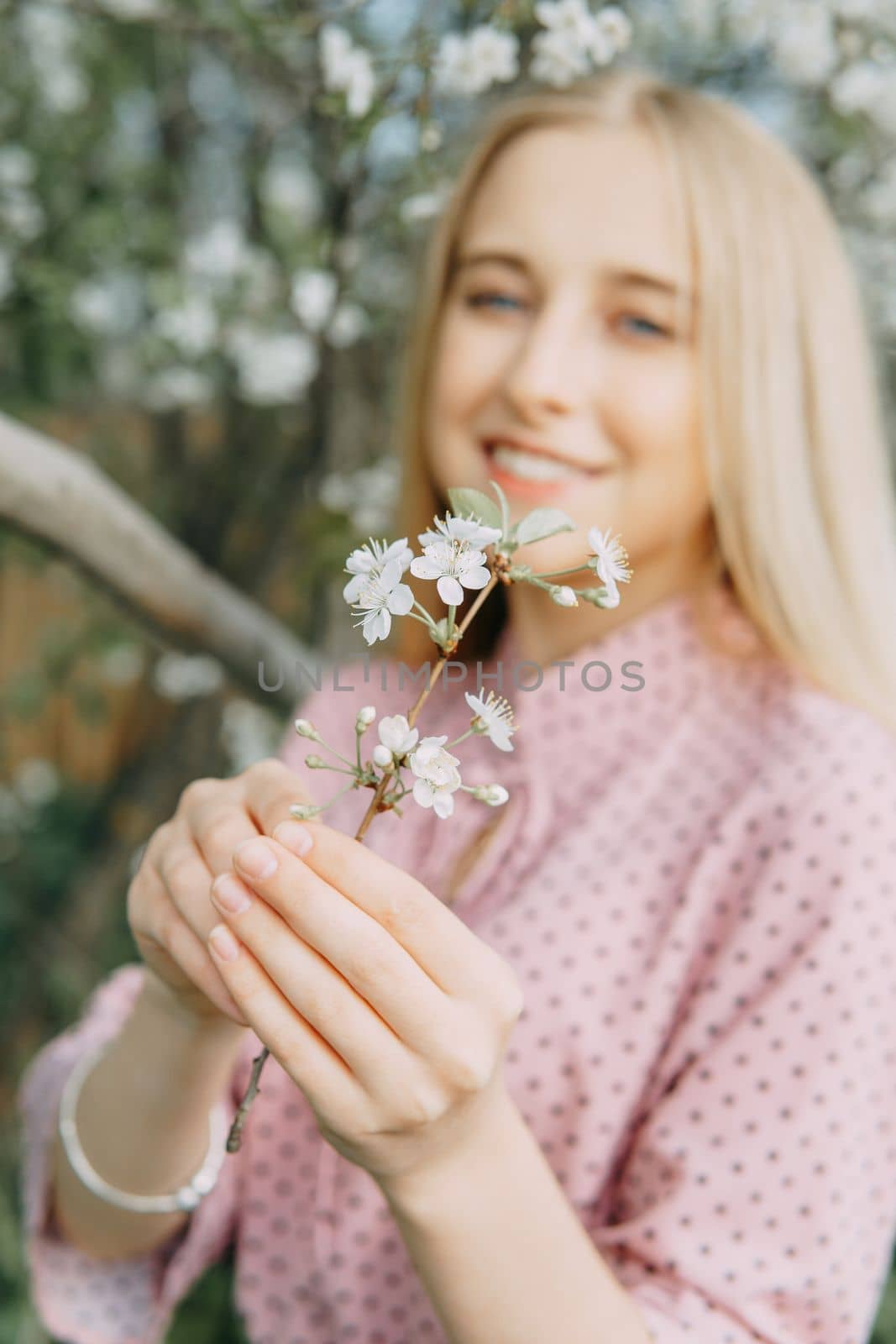 Blonde girl on a spring walk in the garden with cherry blossoms. Female portrait, close-up. A girl in a pink polka dot dress