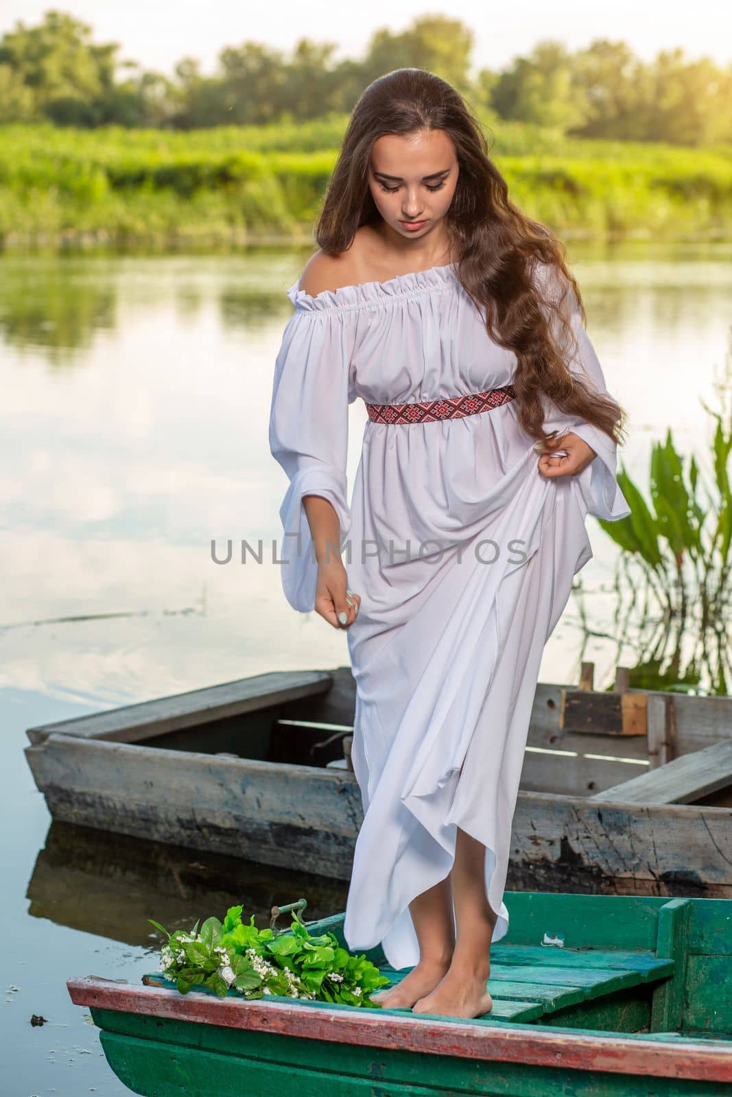 Young sexy woman on boat at sunset. The girl has a flower wreath on her head, relaxing and sailing on river. Fantasy art photography. by nazarovsergey