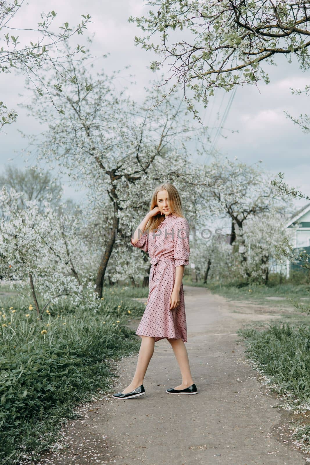 Blonde girl on a spring walk in the garden with cherry blossoms. Female portrait, close-up. A girl in a pink polka dot dress