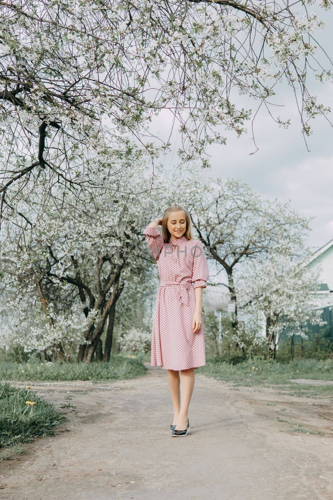 Blonde girl on a spring walk in the garden with cherry blossoms. Female portrait, close-up. A girl in a pink polka dot dress
