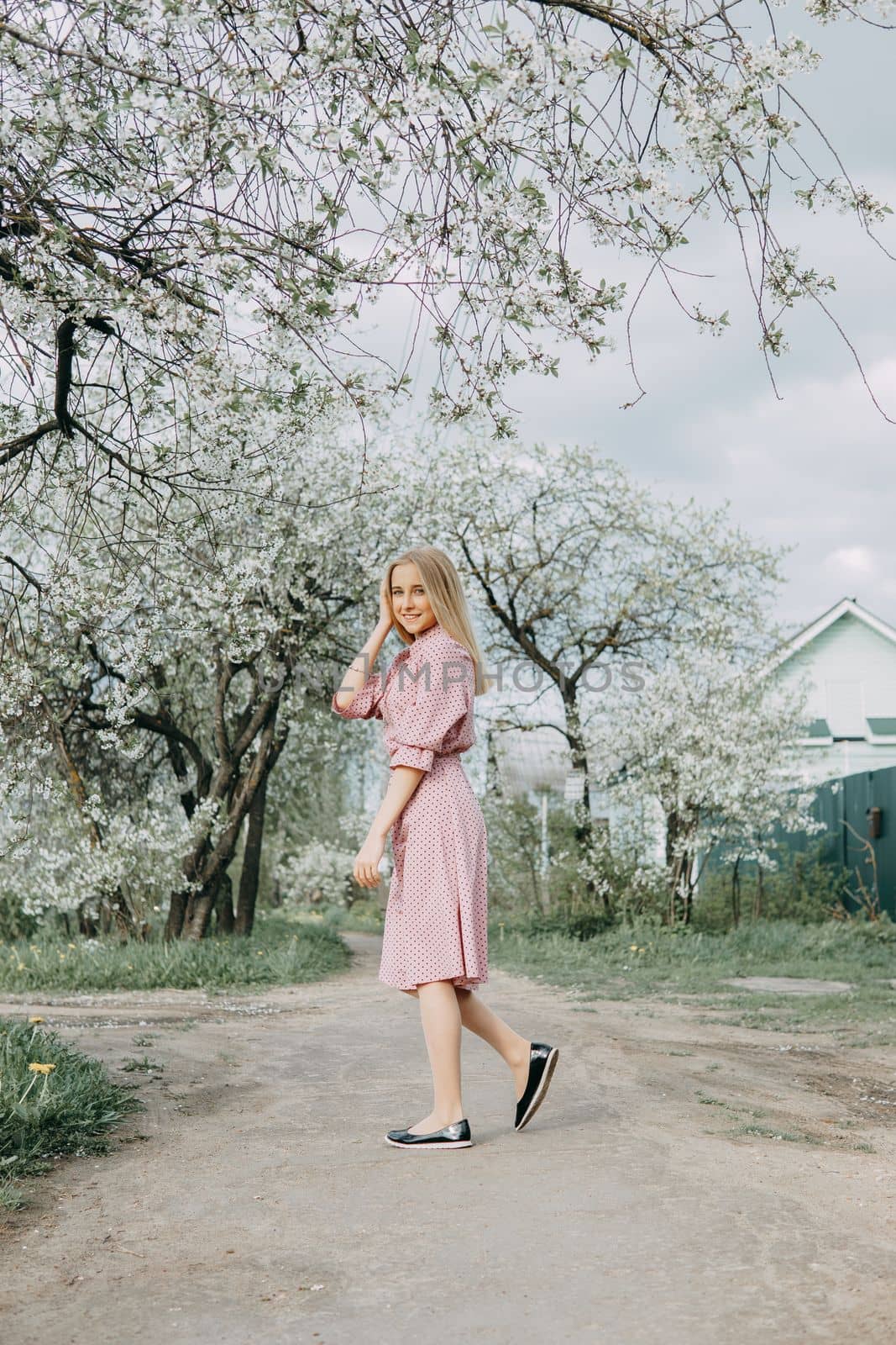 Blonde girl on a spring walk in the garden with cherry blossoms. Female portrait, close-up. A girl in a pink polka dot dress