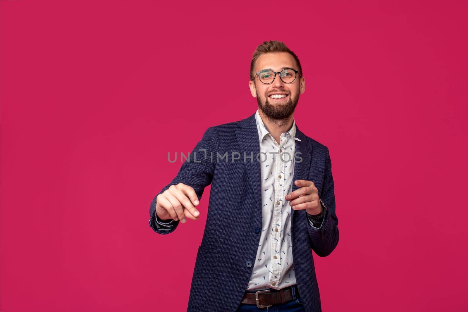 Studio shot of attractive brunette business man with glasses, in casual shirt, stylish black jacket talking, smiling. Isolated pink background.