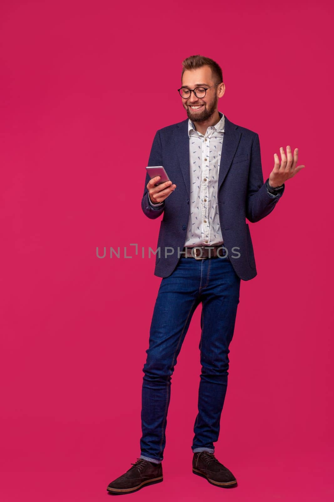 Studio shot of attractive brunette business man with glasses, in casual shirt, stylish black jacket talking on the cell phone and smiling. Isolated pink background.