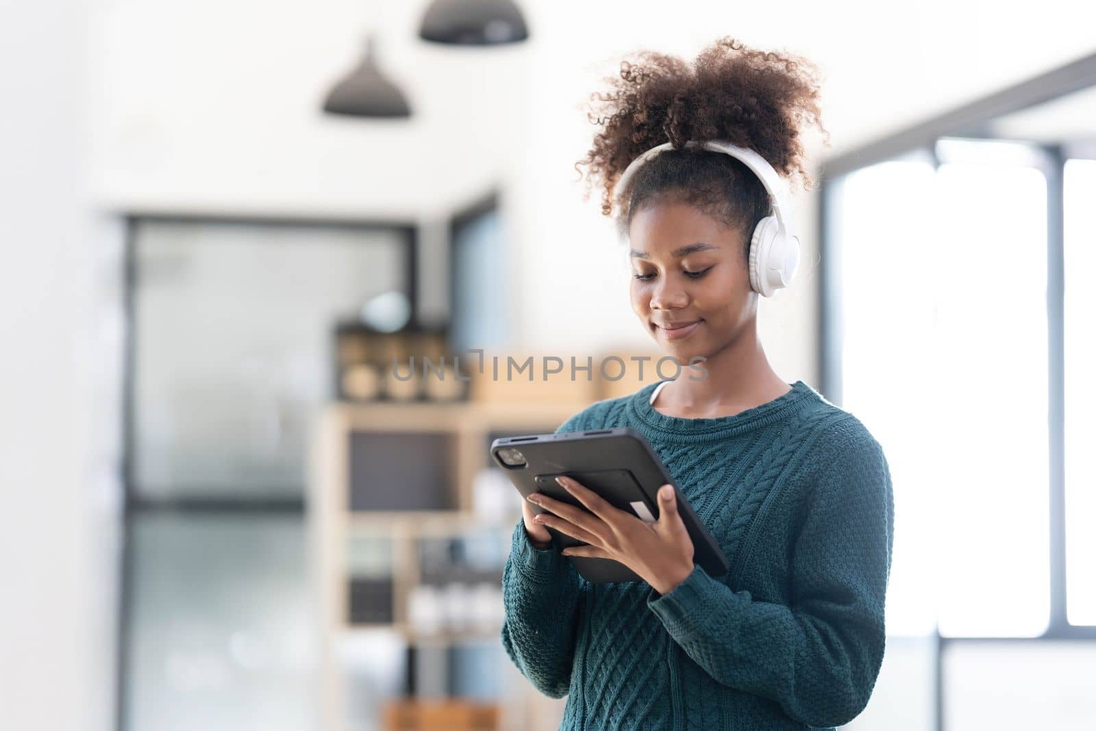 Portrait of smiling young black woman listening music with headset and digital tablet by wichayada