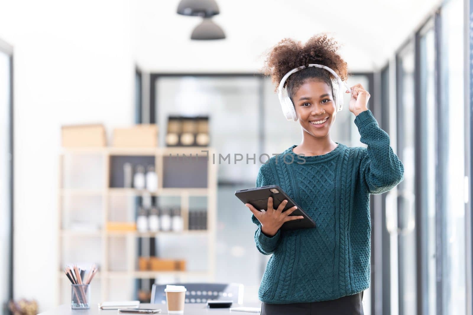 Portrait of smiling young black woman listening music with headset and digital tablet by wichayada