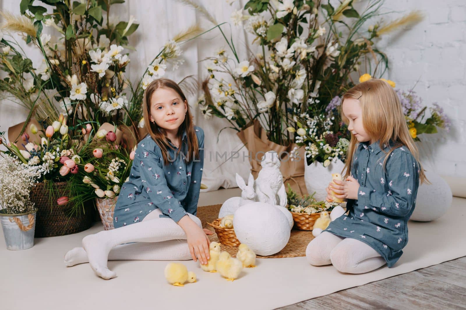 Two girls in a beautiful Easter photo zone with flowers, eggs, chickens and Easter bunnies. Happy Easter holiday