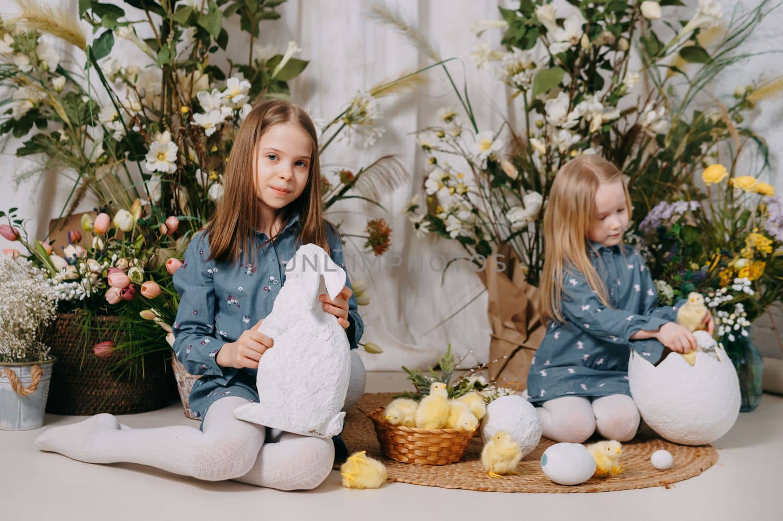 Two girls in a beautiful Easter photo zone with flowers, eggs, chickens and Easter bunnies. Happy Easter holiday