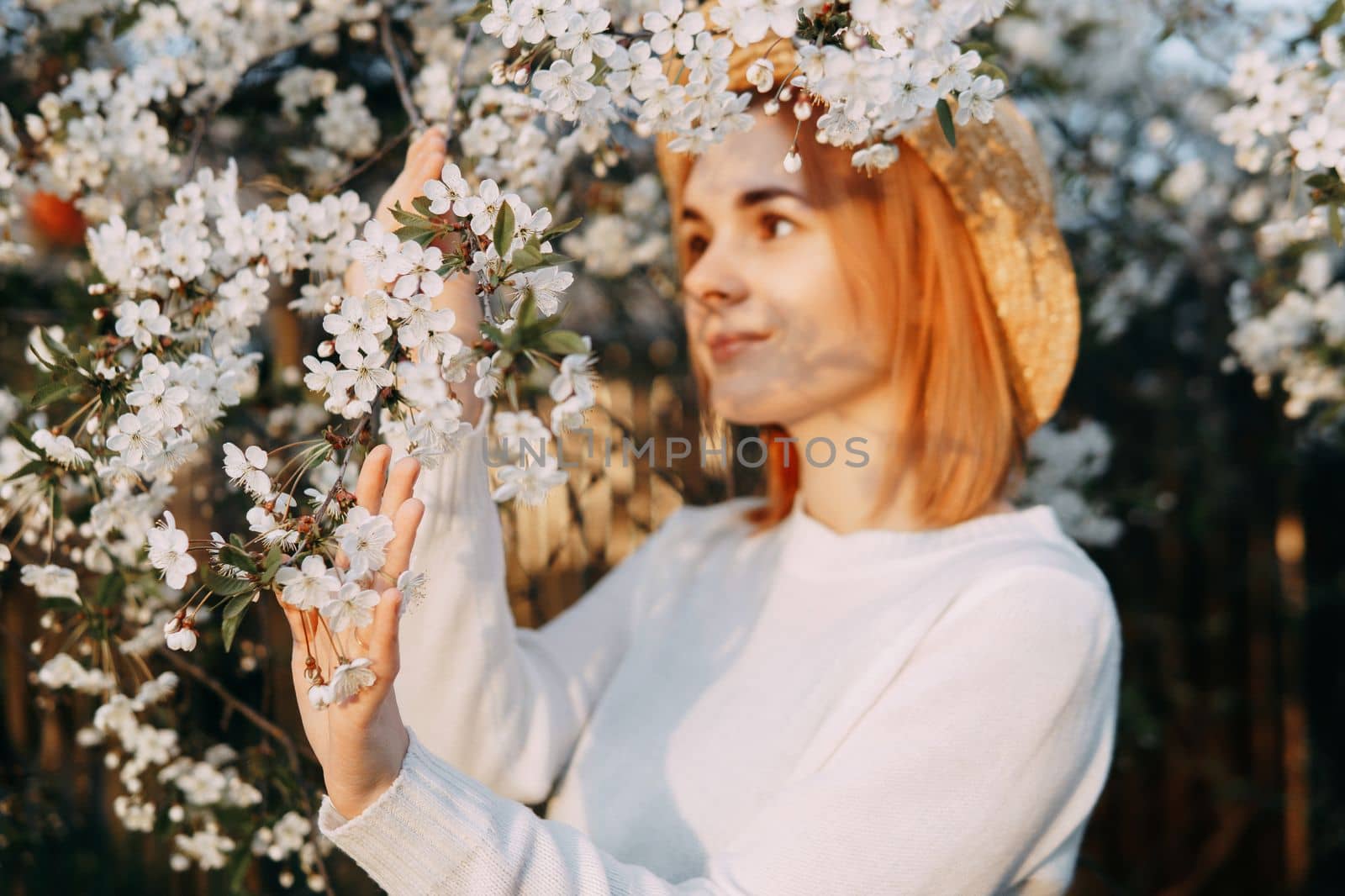 Portrait of a woman in a straw hat in a cherry blossom. Free outdoor recreation, spring blooming garden.
