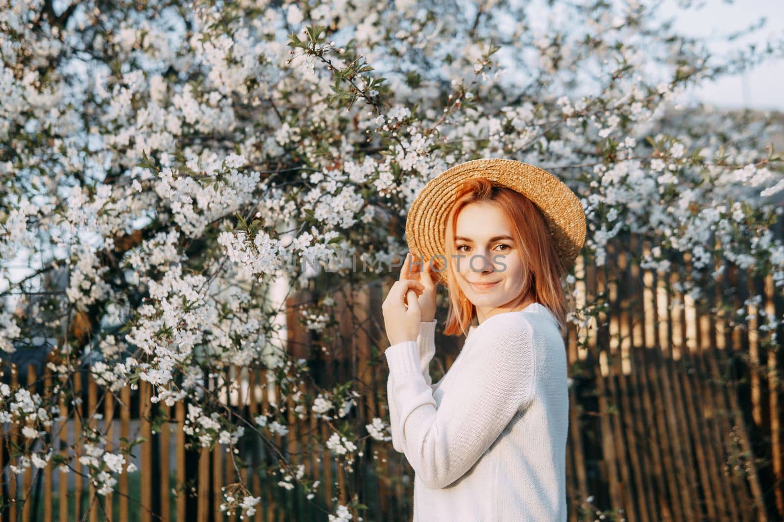 Portrait of a woman in a straw hat in a cherry blossom. Free outdoor recreation, spring blooming garden.