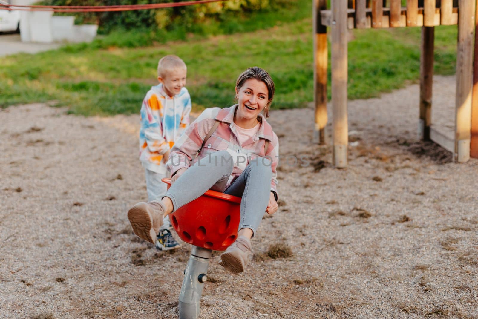 Mother and son having fun on a swing. Motherhood and childhood concept. Sunny summer day. Beautiful family is having fun outside. Parents with children riding on a swing. Mom is playing with her little son on a terrace with swings. A mother woman swings on a swing in the park. Mom and child are on a swing in nature by Andrii_Ko