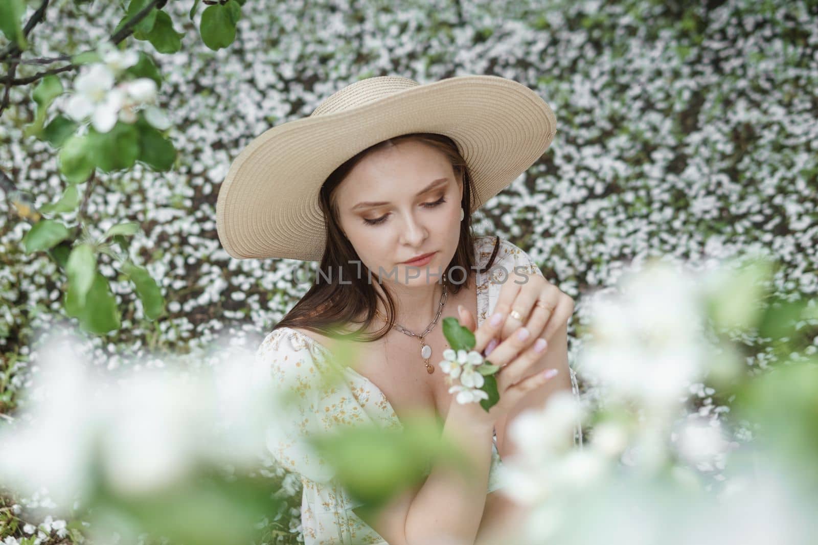 An attractive long-haired woman walks in the spring in the park of blooming apple trees. Spring portrait of a woman