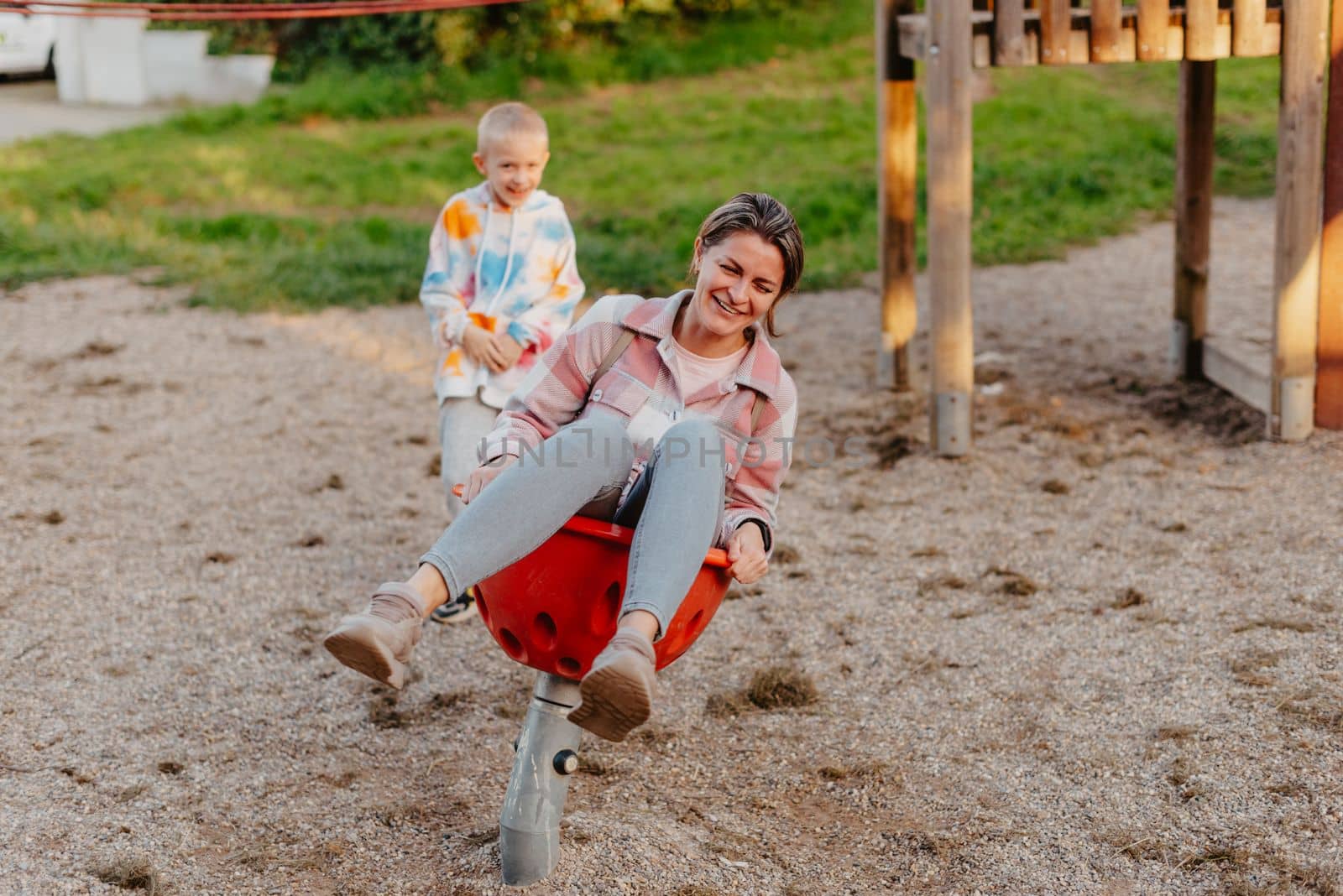 Mother and son having fun on a swing. Motherhood and childhood concept. Sunny summer day. Beautiful family is having fun outside. Parents with children riding on a swing. Mom is playing with her little son on a terrace with swings. A mother woman swings on a swing in the park. Mom and child are on a swing in nature