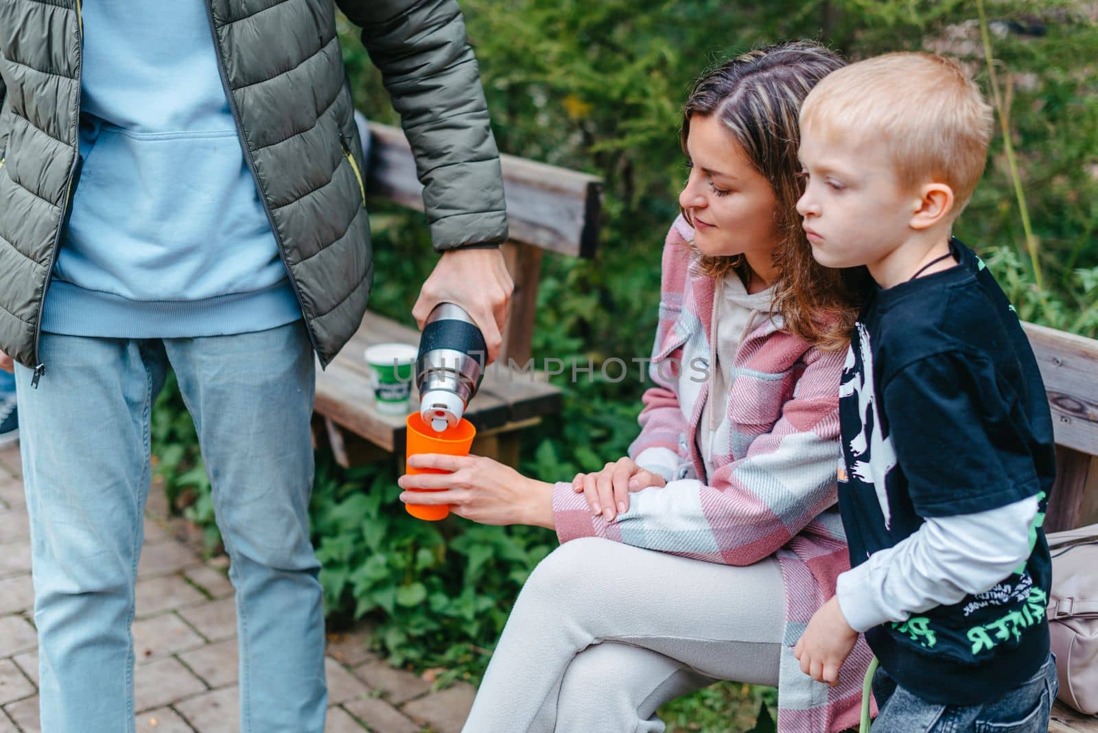 Happy Family drinking tea from a thermos in the forest. Photo of cute charming mother with childrens dressed casual outfit walking sitting bench drinking tea smiling outside city park by Andrii_Ko