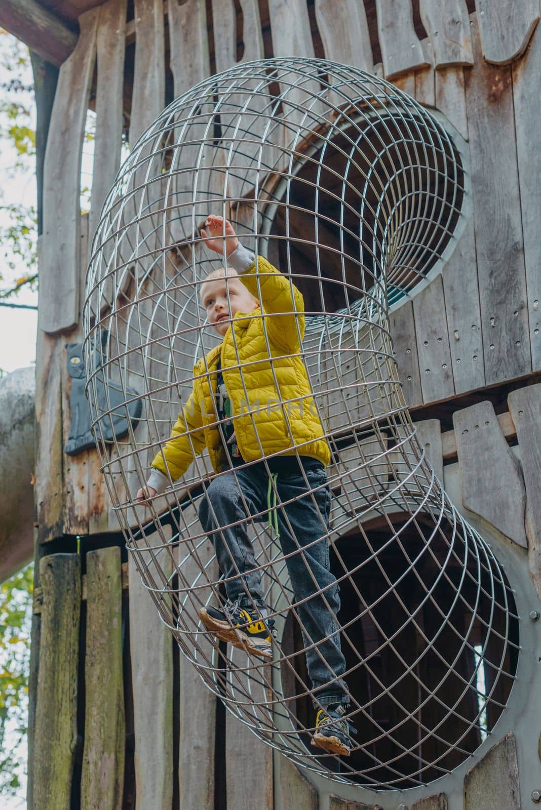 A child climbs up an alpine grid in a park on a playground on a hot summer day. children's playground in a public park, entertainment and recreation for children, mountaineering training. Child playing on outdoor playground. Kids play on school or kindergarten yard. Active kid on colorful slide and swing. Healthy summer activity for children. Little boy climbing outdoors. by Andrii_Ko