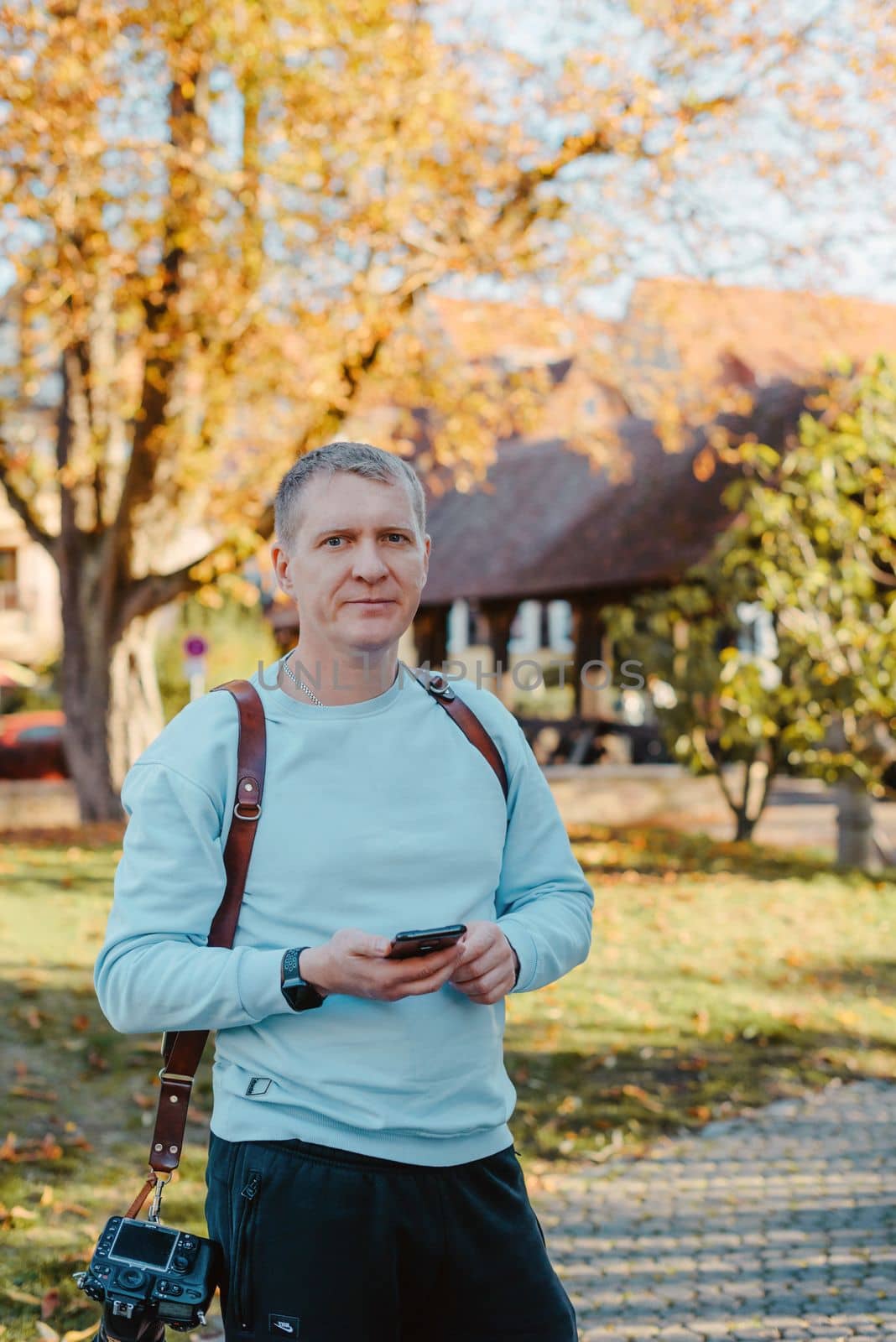 Professional Photographer Taking Picture Of Beautiful Autumn Park. Man Professional Photographer standing With Camera And With Smartphone In Autumn Park. Retouched, Vibrant Colors by Andrii_Ko