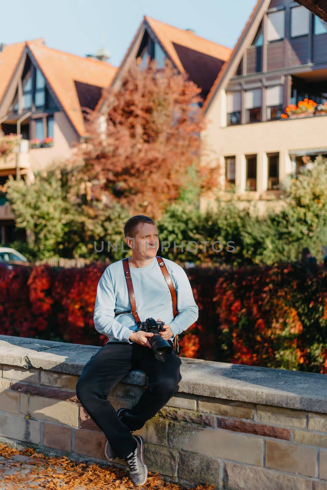 Man Sitting in Old European City And Holding Photo Camera. Contemporary Stylish Blogger And Photographer. Handsome man taking a selfie on a trip in Europe. by Andrii_Ko