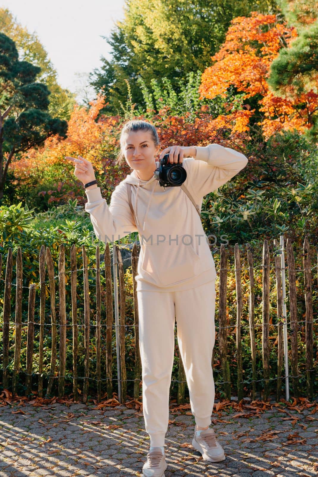 Beautiful young woman takes photos with a professional camera in autumn forest. Smiling girl enjoying autumn weather. Rest, relaxation, lifestyle concept. Young photographer takes pictures of autumn forest at sunset