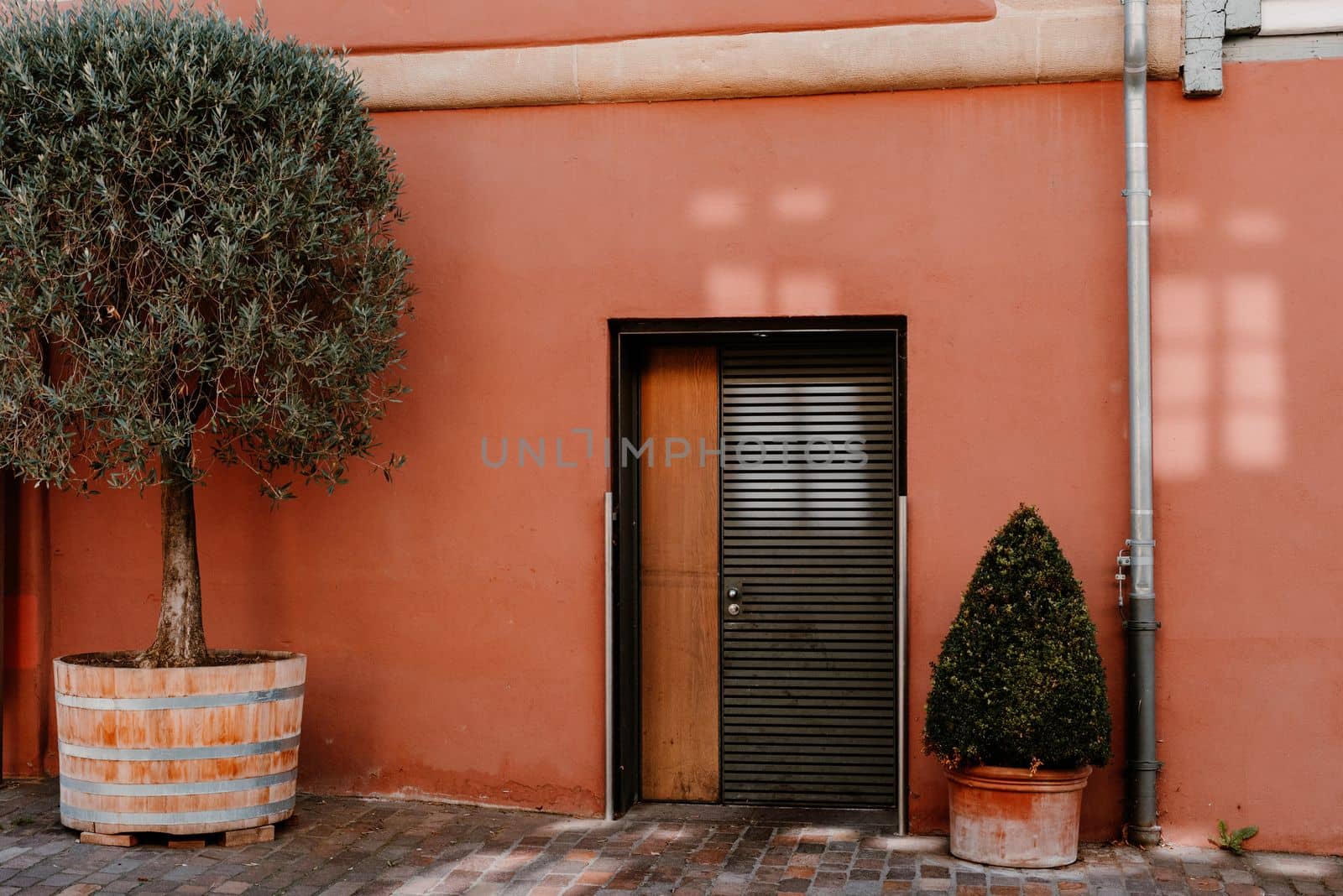 Facade of a modern house with a gray front door and potted flowers. Old historic Italian architecture. Traditional European old town building. Blue wooden door, balcony, blooming bush, pastel walls with sunlight shadows. Aesthetic summer vacation travel background