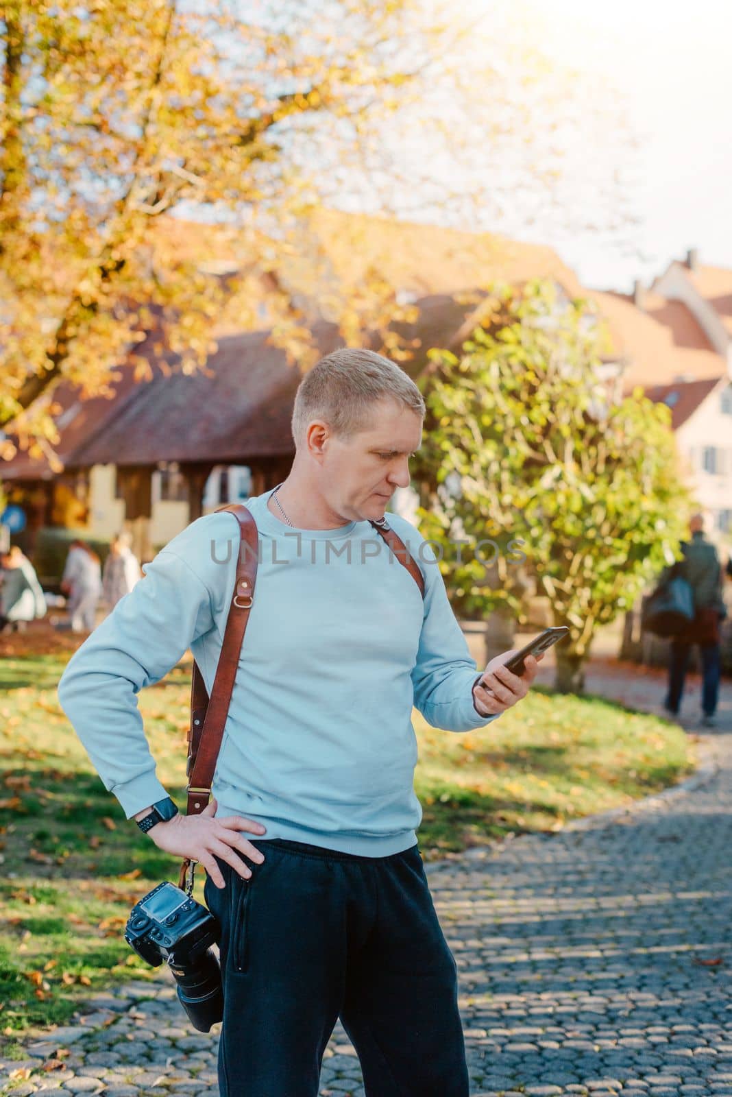 Professional Photographer Taking Picture Of Beautiful Autumn Park. Man Professional Photographer standing With Camera And With Smartphone In Autumn Park. Retouched, Vibrant Colors by Andrii_Ko