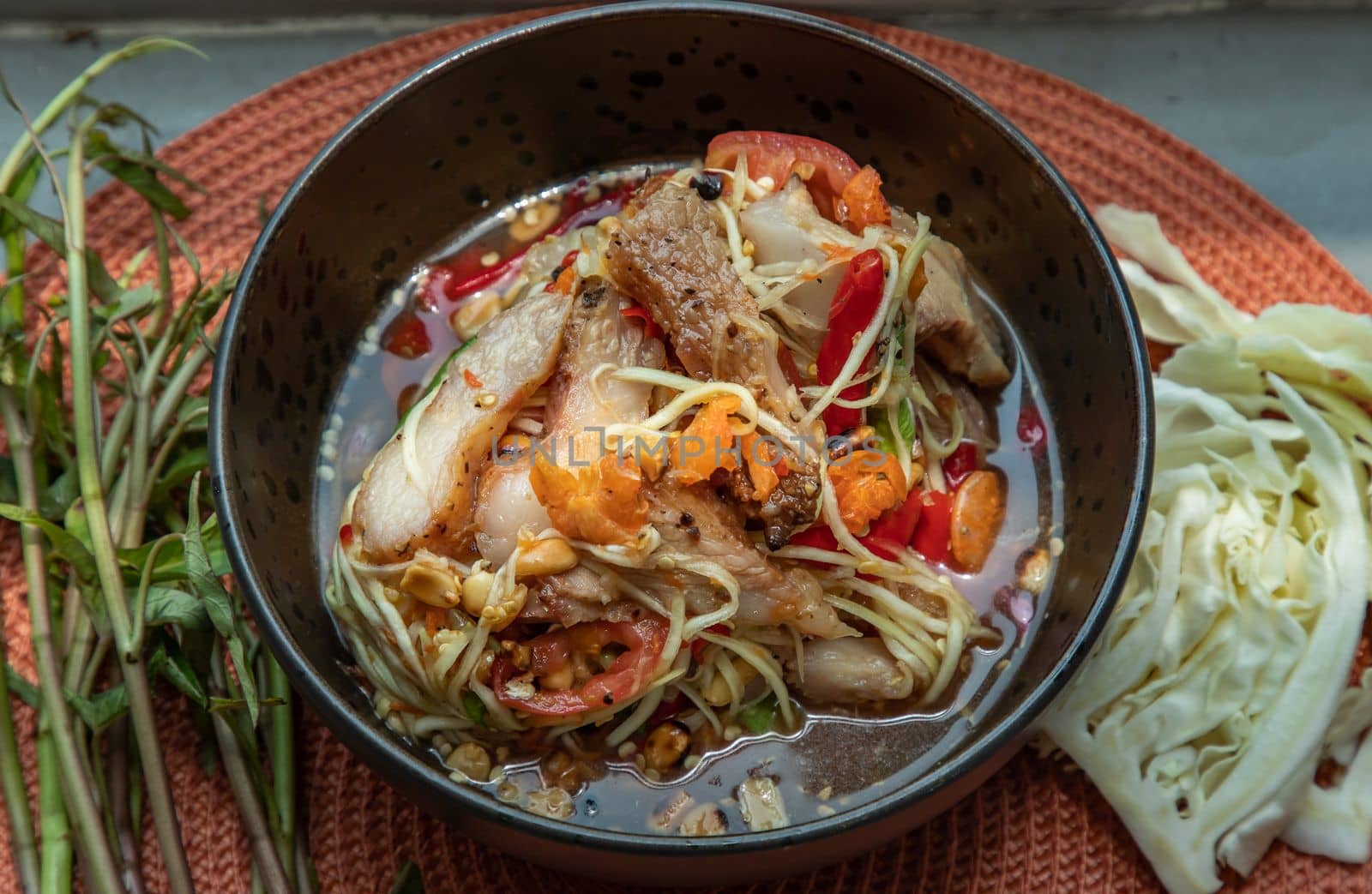 Thai papaya spicy salad (som tum) mix grilled pork neck on ceramic dishes. delicious spicy Thai food, Selective focus.