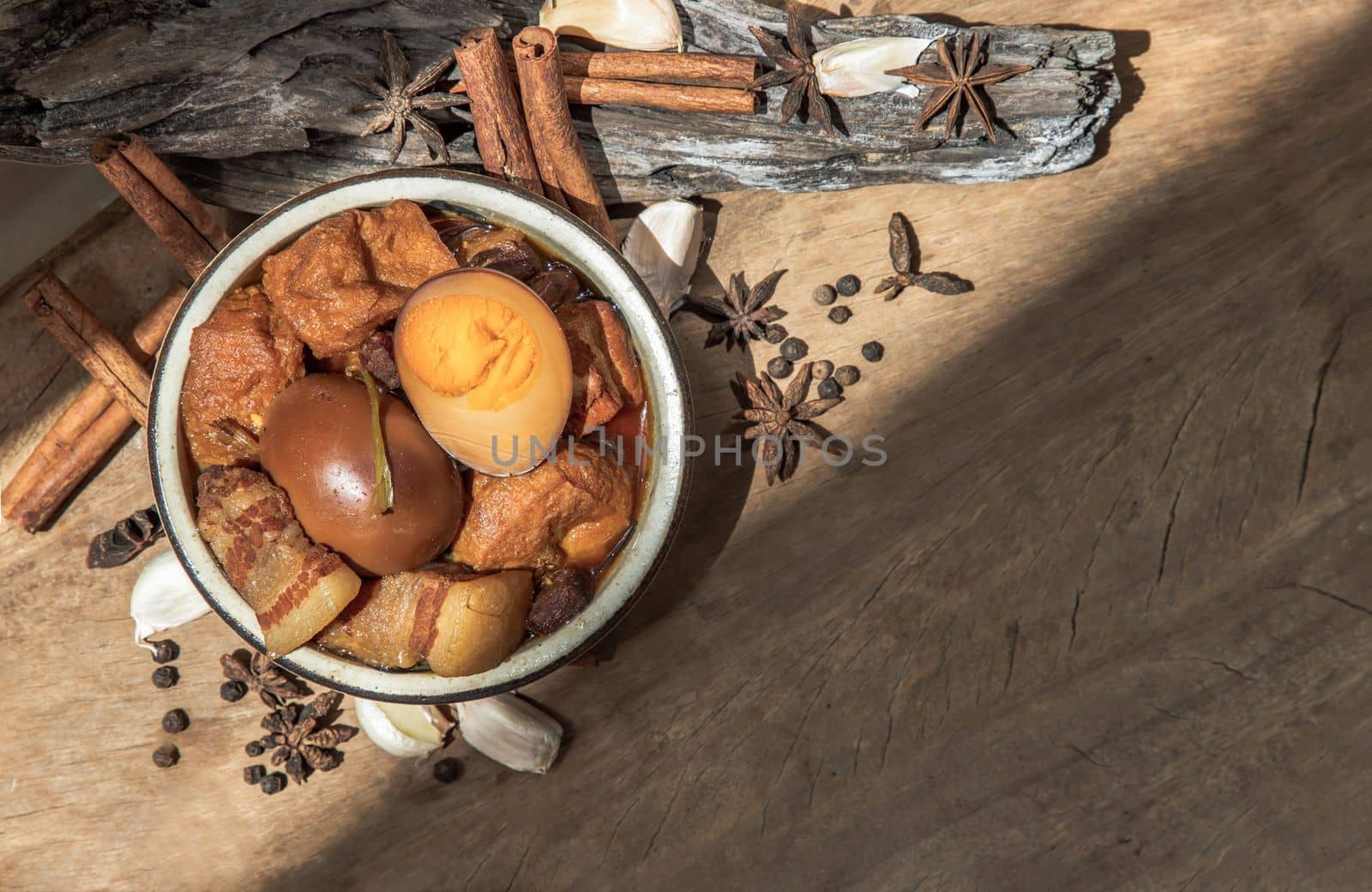 Boiled egg (kai pa lo) and Belly Pork Chinese Five-Spice Stewed with Tofu in brown sauce decorated with anise star, cinnamon, garlic and black pepper on old wooden table, Asia food, Top view, Copy space, Selective focus.
