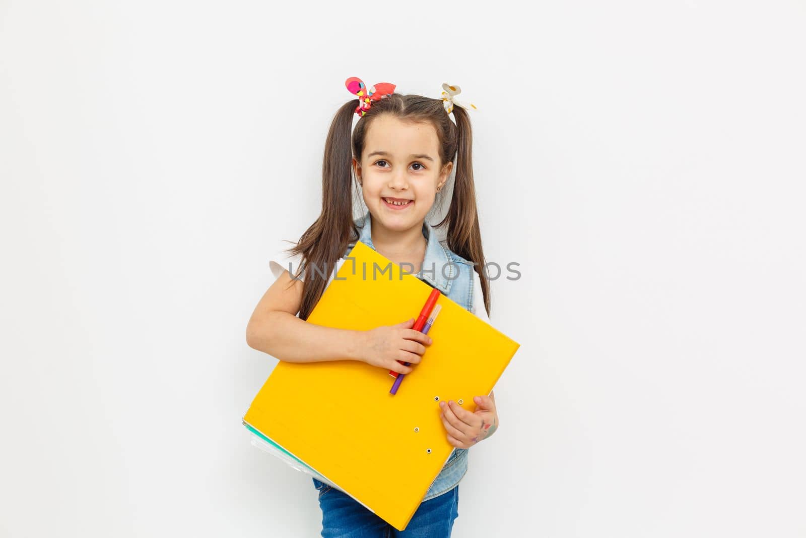 a cute little girl with two tails is holding a folder with papers in her hands. returning to school