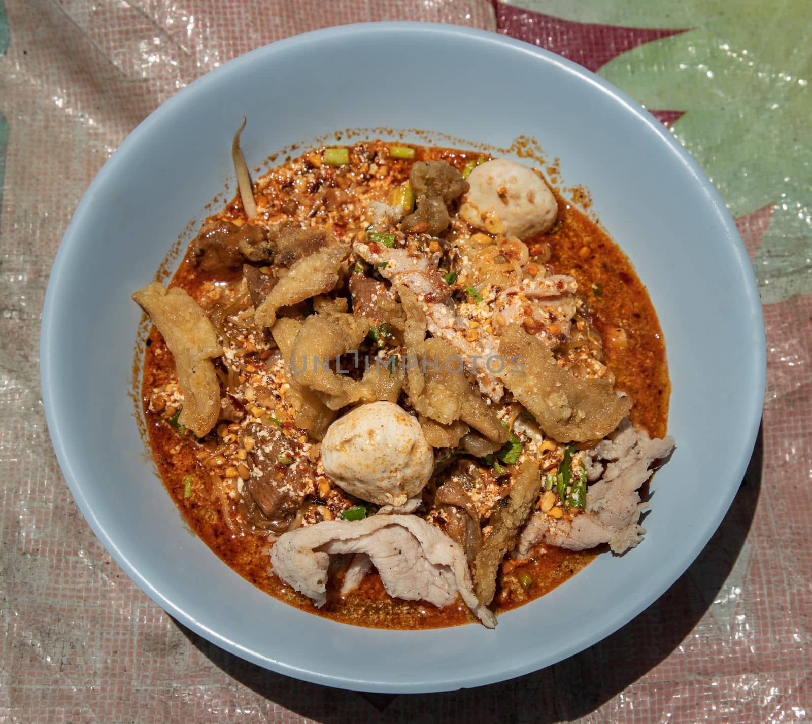 Egg noodles in Thai spicy soup with braised pork, pork balls and fatty pork rinds in blue bowl. Thai food, Top view, Selective focus.