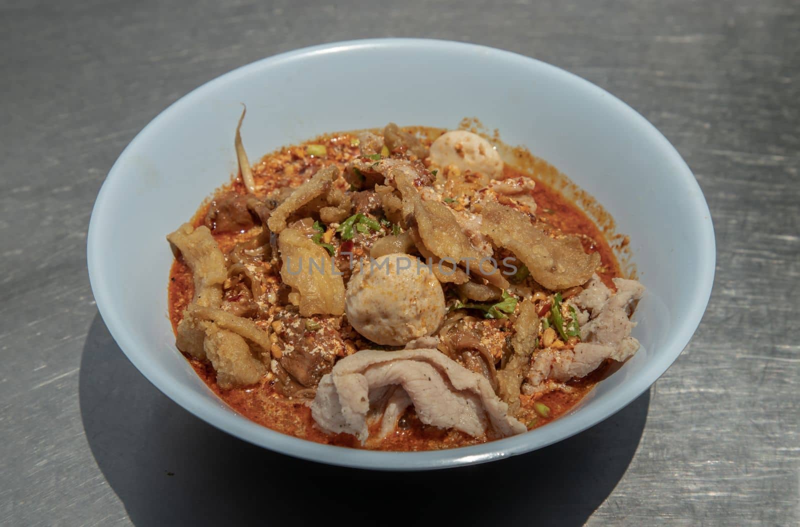 Egg noodles in Thai spicy soup with braised pork, pork balls and fatty pork rinds in white bowl. Thai food, Selective focus.