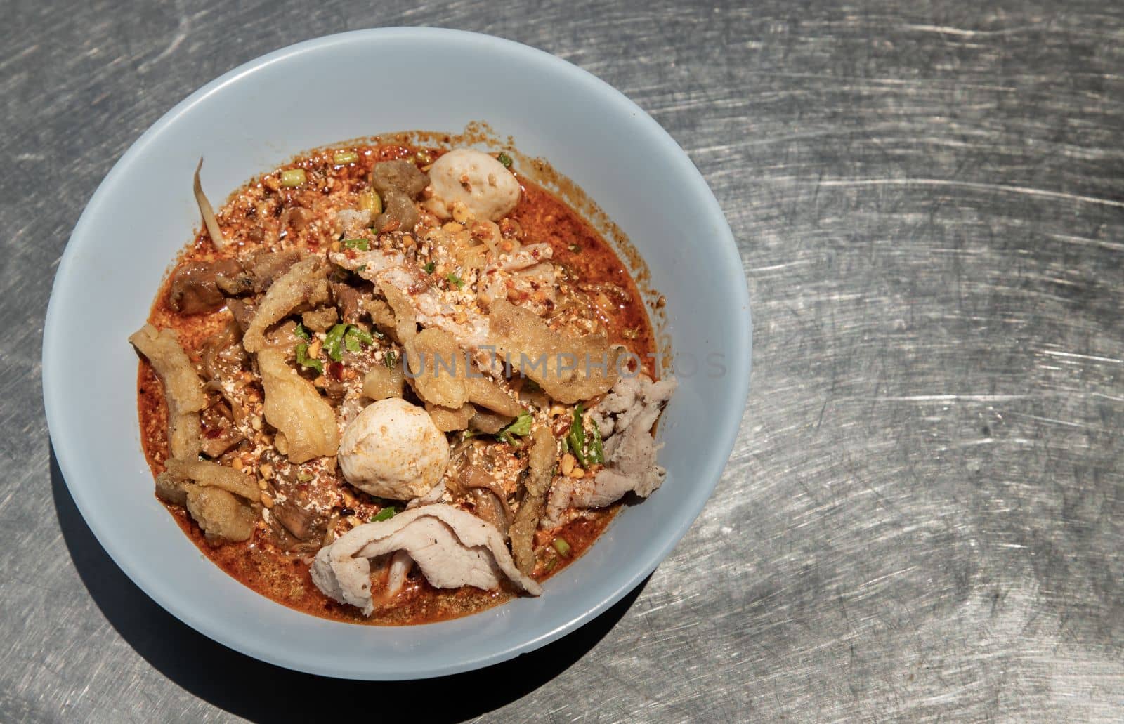 Egg noodles in Thai spicy soup with braised pork, pork balls and fatty pork rinds in white bowl. Thai food, Top view, Selective focus.