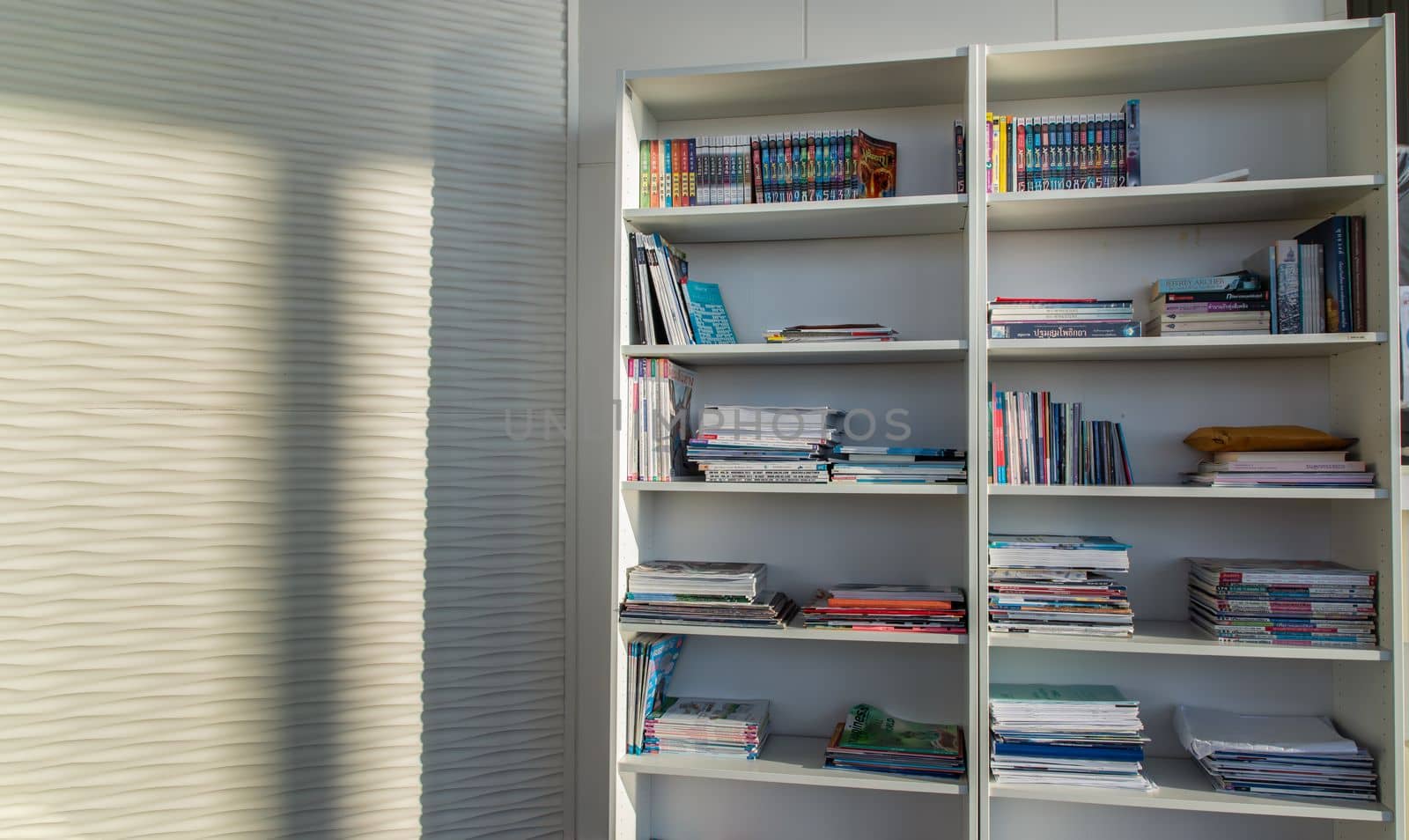 Bangkok,Thailand - Jan 10, 2022 : Library of shared facility at living room of home condominium. Different books are arranged on a white bookshelf, Selective focus.