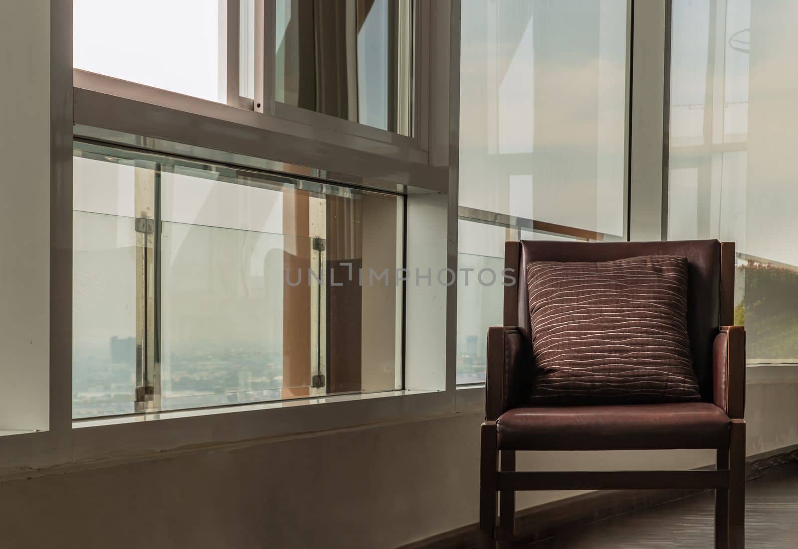 Bangkok, Thailand - Jan 10, 2022 : Brown leather armchair with pillow near the glass window in common area. Working space with Space for text, Selective focus.