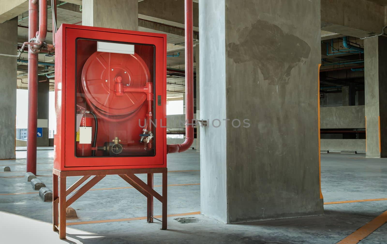 A red fire fighting equipment cabinet or fire extinguishing cabinet of fire protection set is located in car parking. Emergency Fire Extinguisher, Rolled Pipe, Hydrant and water hoses, Safety first concept. Selective focus.