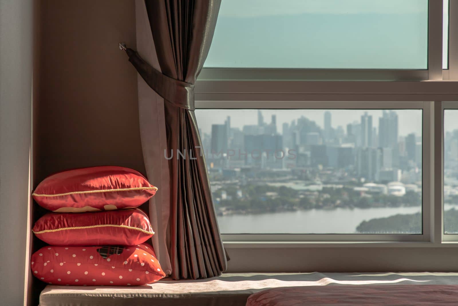Three red Pillows in the corner on Sofa bed with Curtain near Glass window with city view. Landscaped Resting Area for people who living in lifestyle, Copy space, Selective focus.