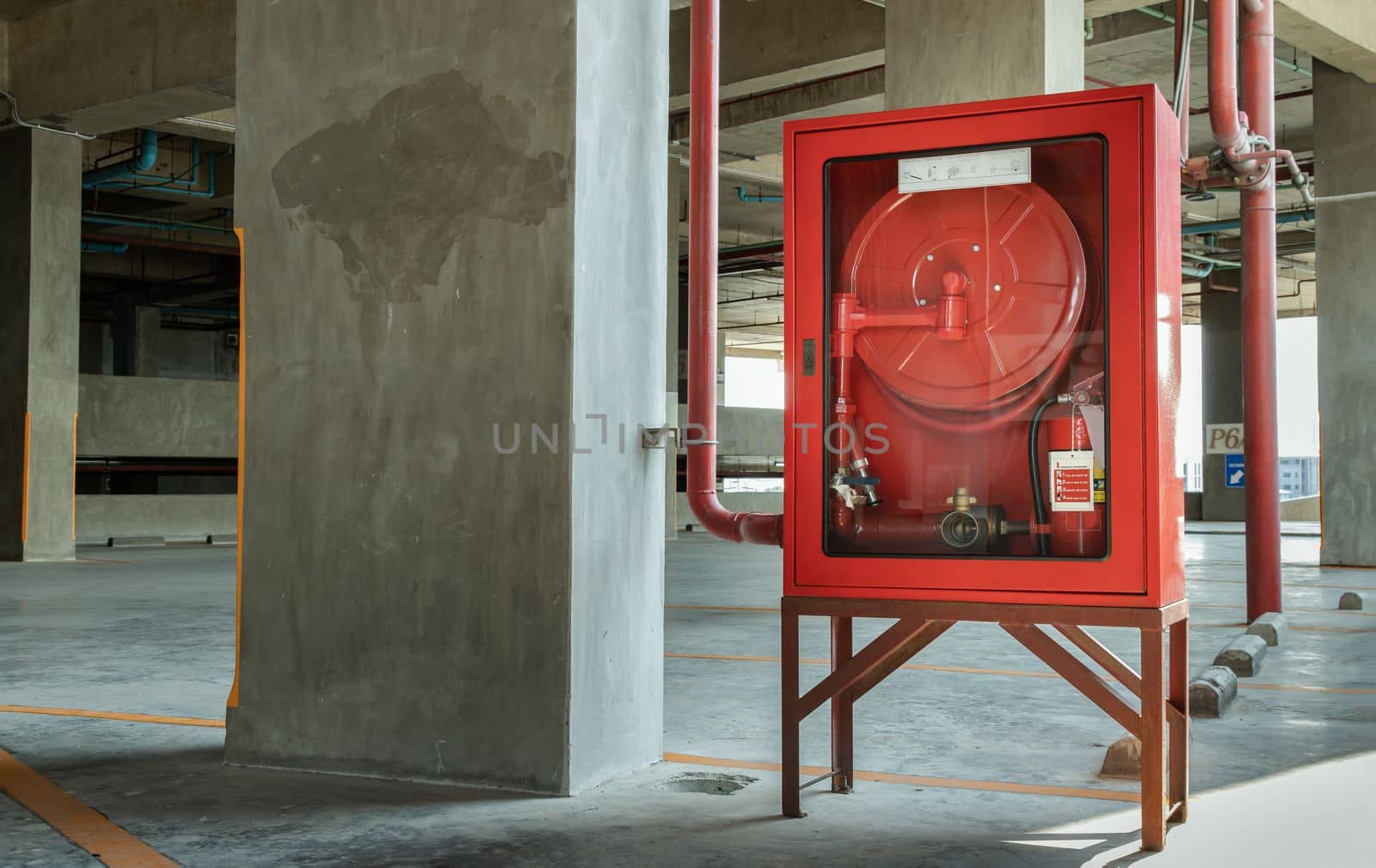 A red fire fighting equipment cabinet or fire extinguishing cabinet of fire protection set is located in car parking. Emergency Fire Extinguisher, Rolled Pipe, Hydrant and water hoses, Safety first concept. Selective focus.