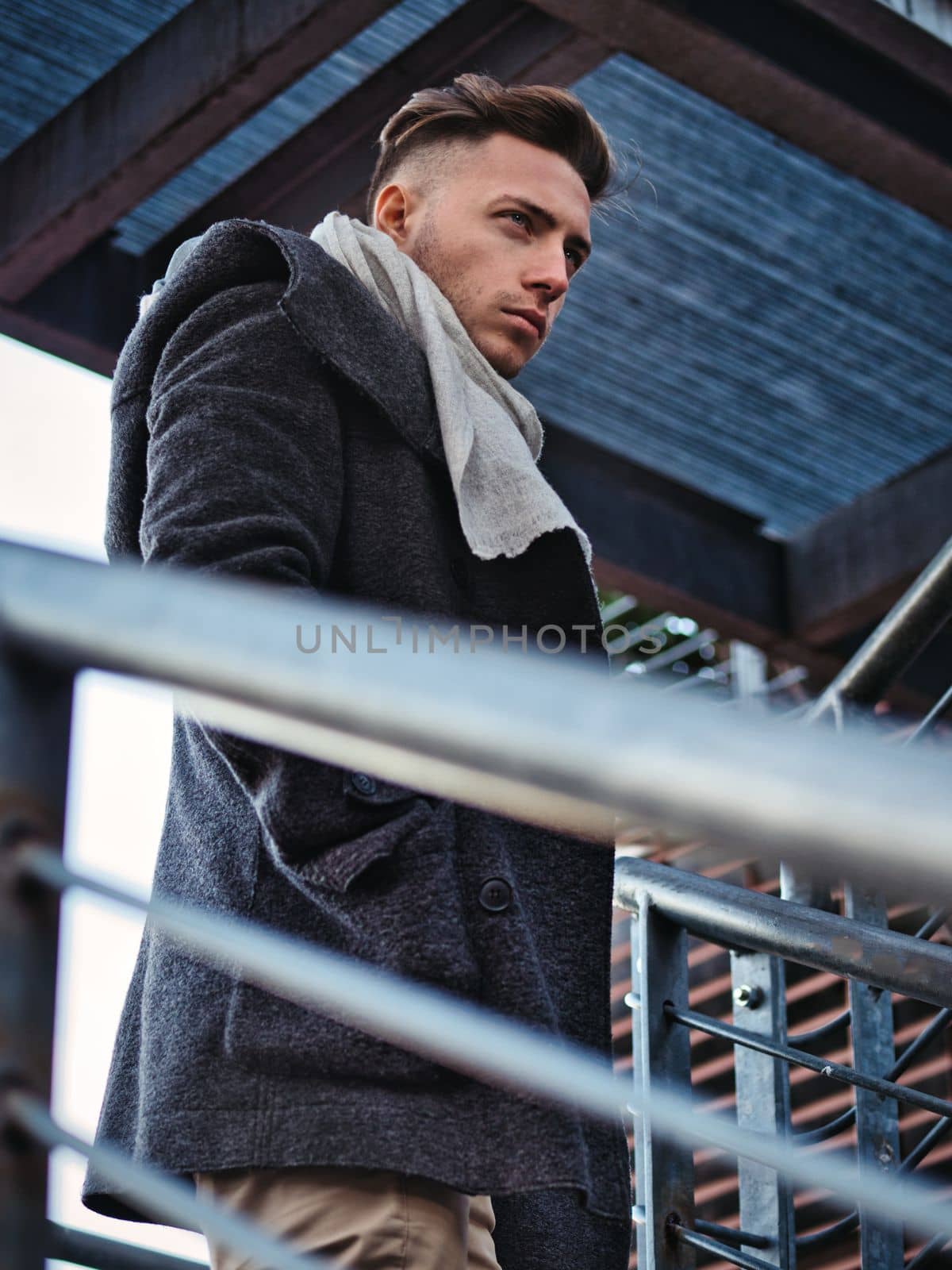 One handsome young man in urban setting in moden city, standing, wearing black coat and scarf in winter day