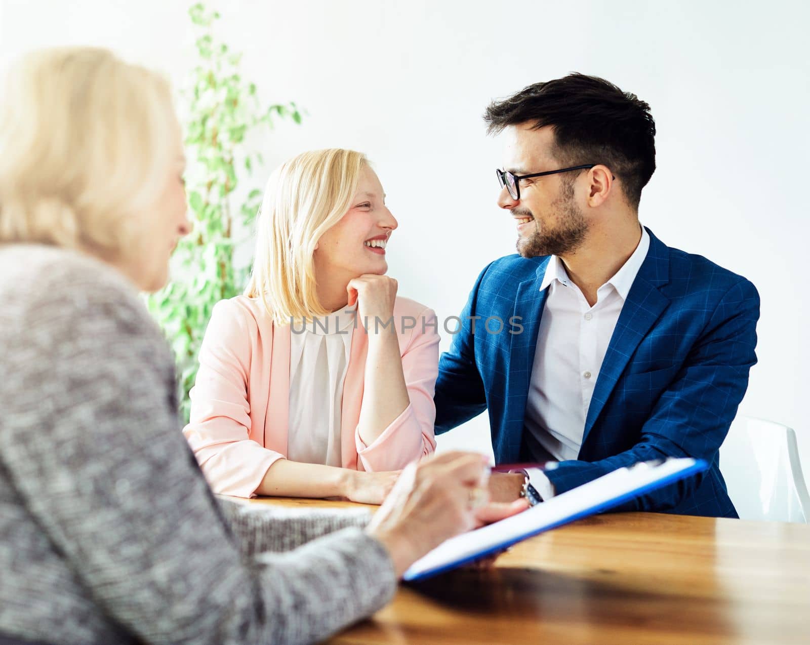 Young happy couple and an agent in a new property or in the office signing a deal and showing it