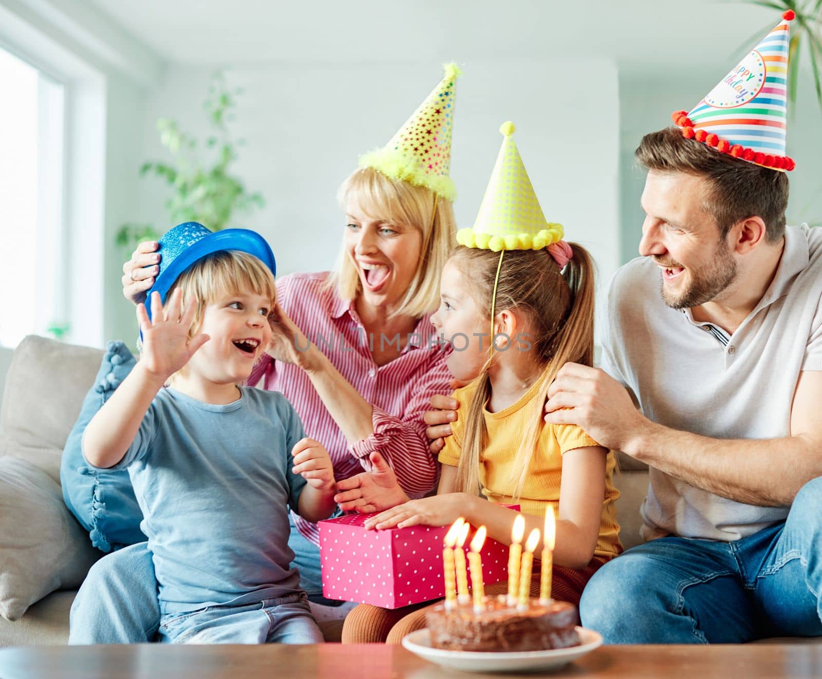 Family of four, mother, father, daughter and son having fun celebrating a birthday together with birthday cake and candles and a present at home