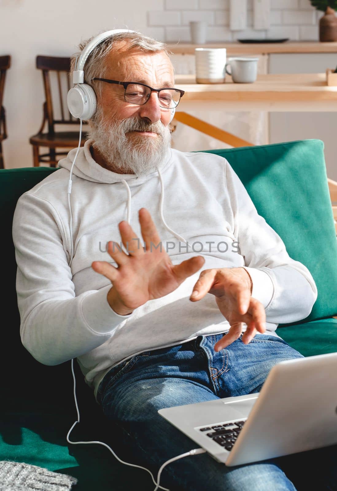 Elderly man making video call on laptop in room waving to screen and chatting with children - modern technologies communication internet