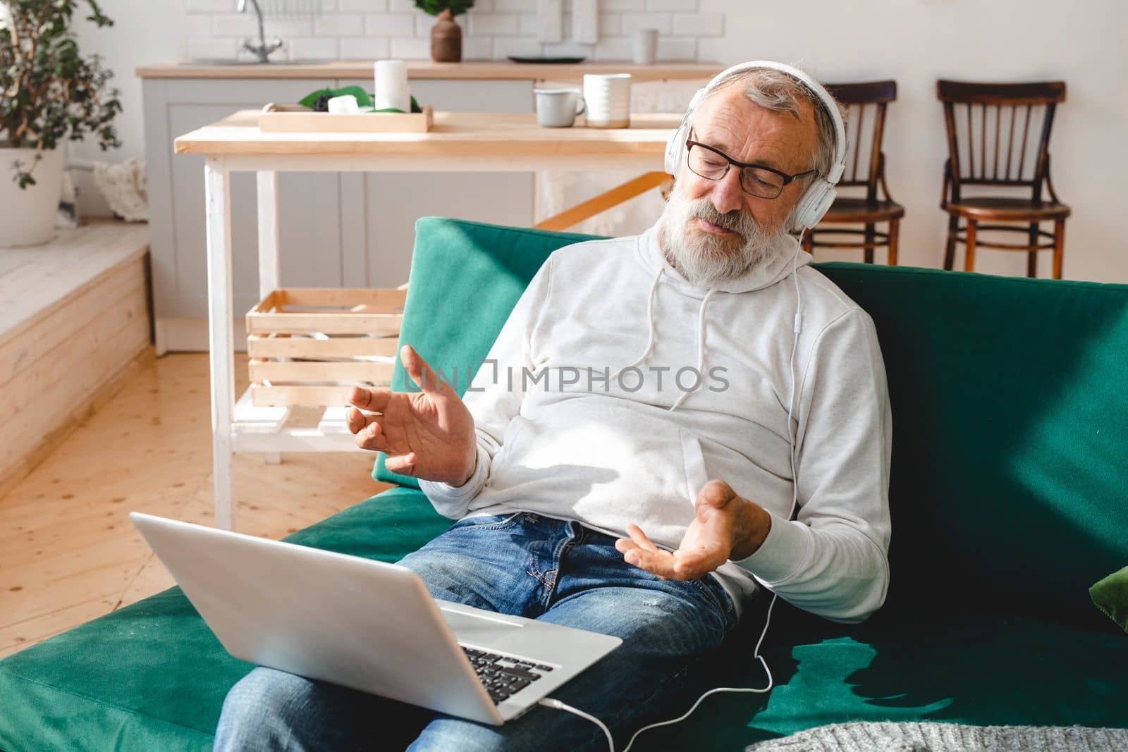 Elderly man making video call on laptop in room waving to screen and chatting with children - modern technologies communication internet