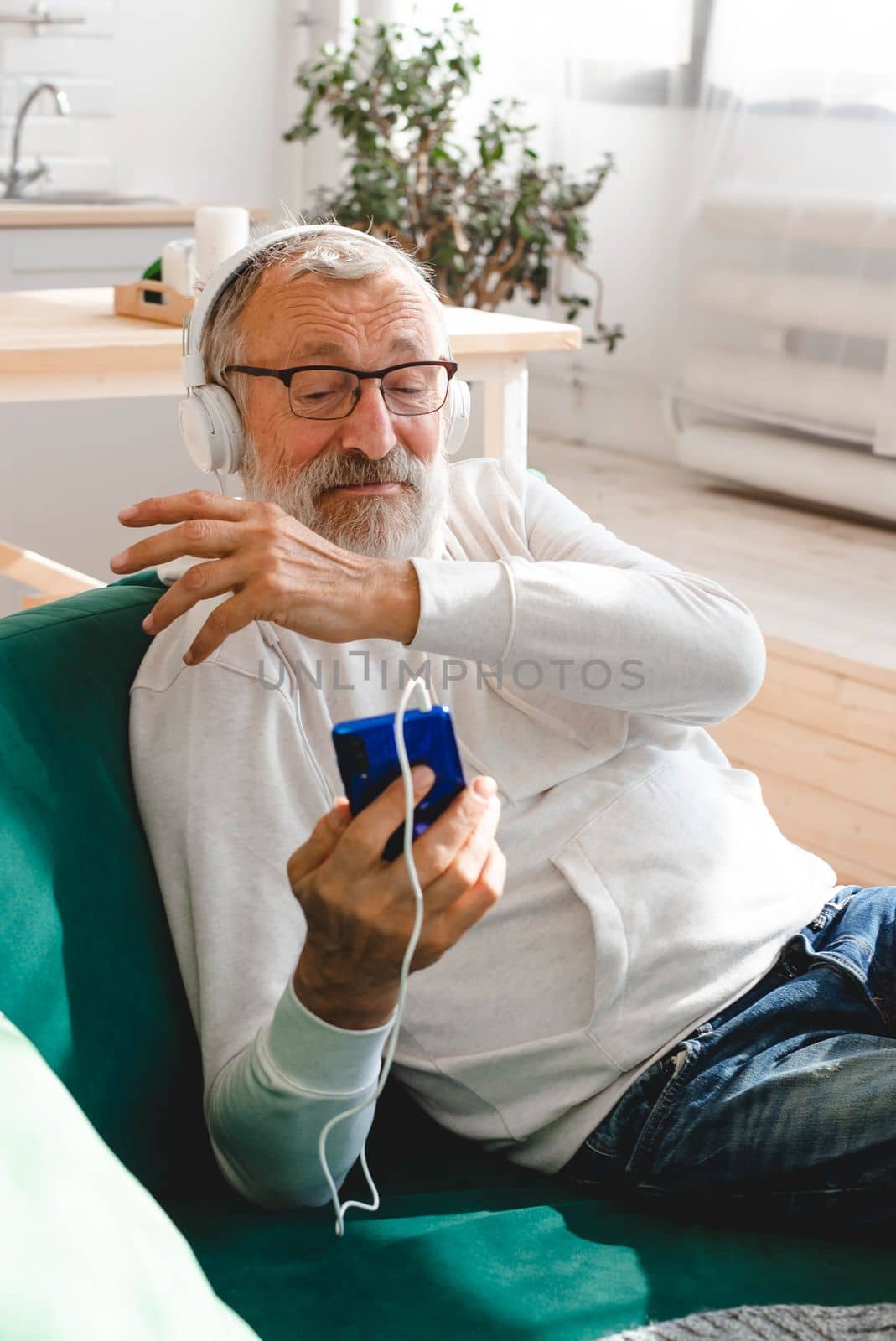 Elderly man cool bearded old man using mobile phone for video call - happiness elderly lifestyle people concept. Video call on smartphone in room waving to screen and chatting with children - modern technologies communication and internet.