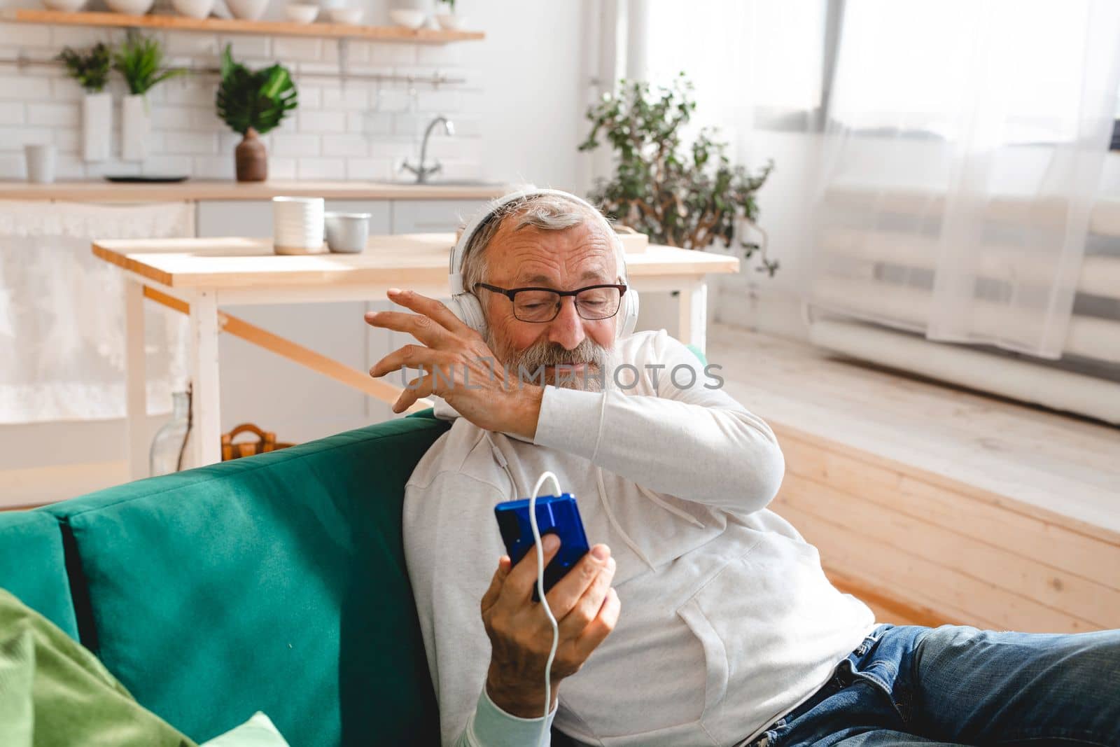 Elderly man making video call on laptop in room waving to screen and chatting with children - modern technologies communication internet