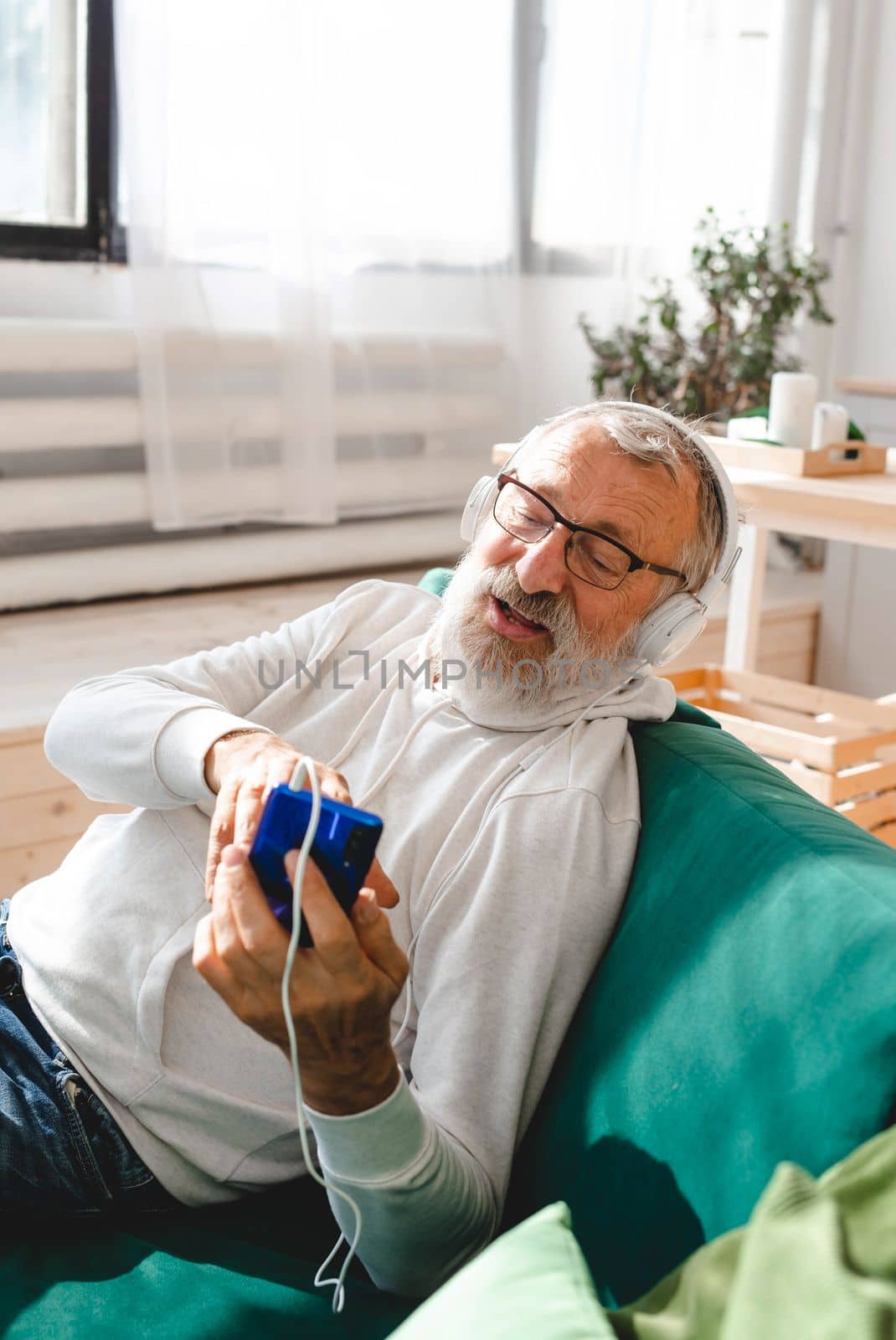 Elderly man cool bearded old man using mobile phone for video call - happiness elderly lifestyle people concept. Video call on smartphone in room waving to screen and chatting with children - modern technologies communication and internet.