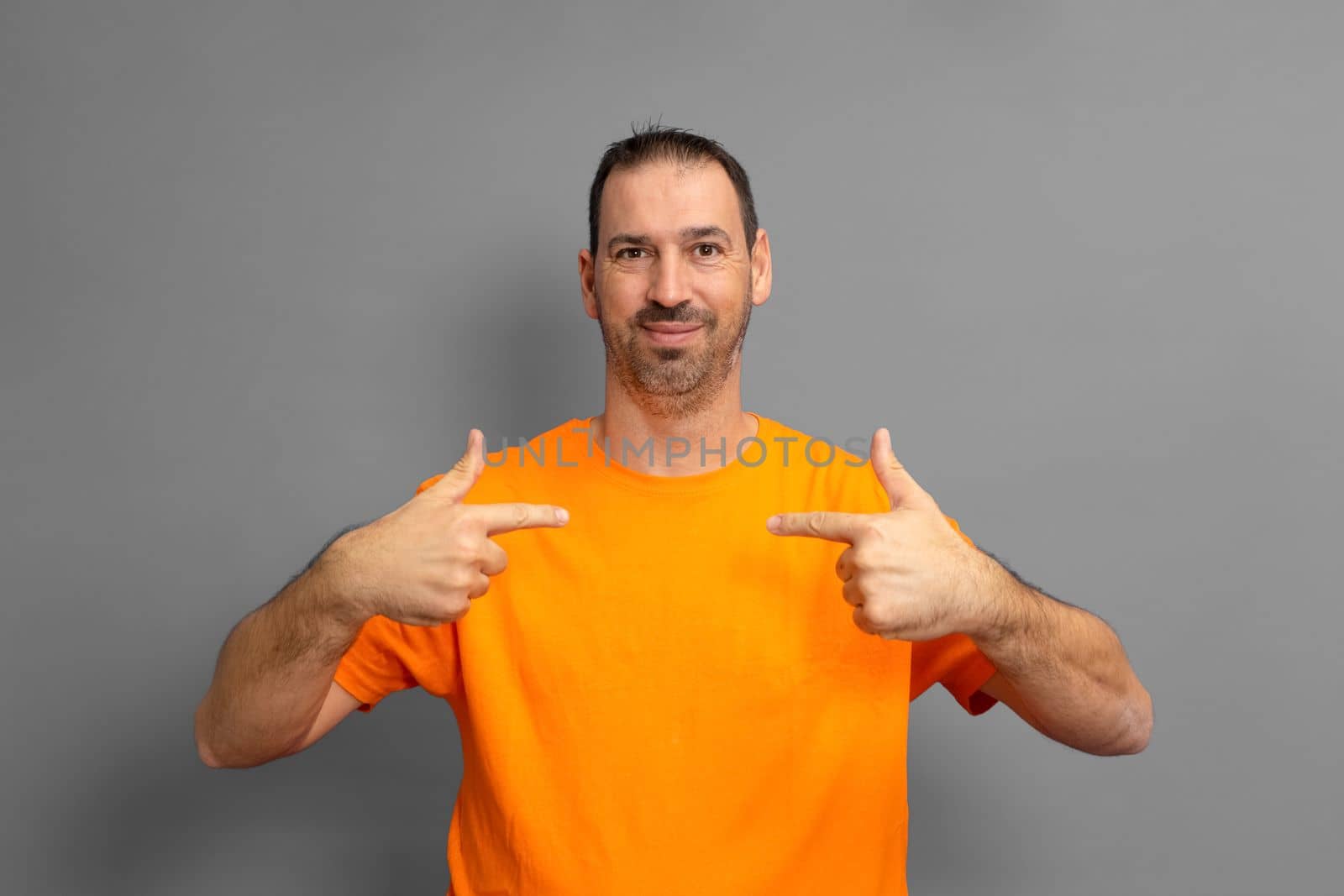 Portrait of handsome Hispanic bearded man pointing to himself puzzled at being chosen. Amazed attractive european man over gray background, he has a confused expression. Surprise concept