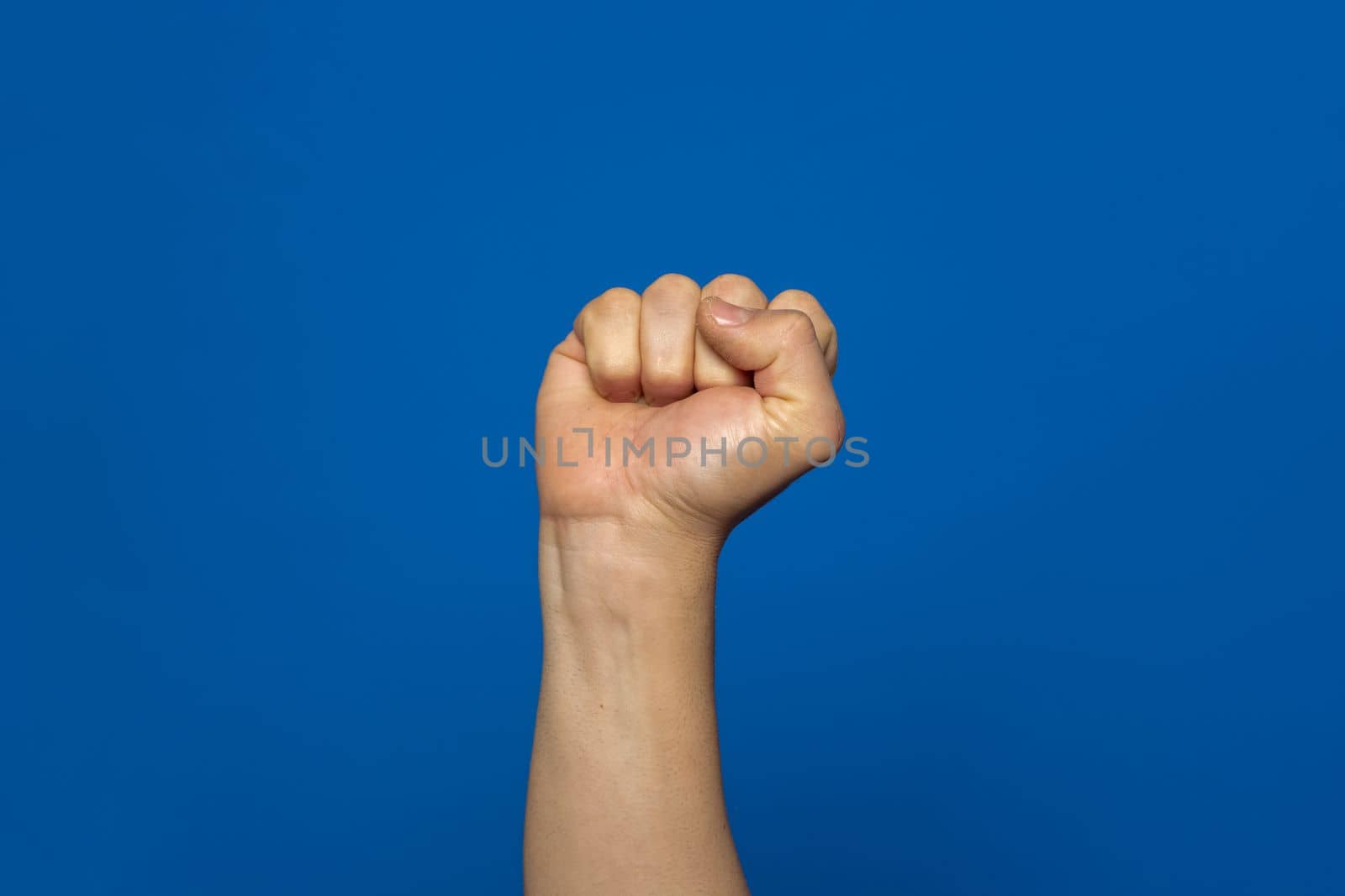 Man's fist seized with power isolated on blue background. Symbol of rebellion and uprising of the working classes oppressed by the elites