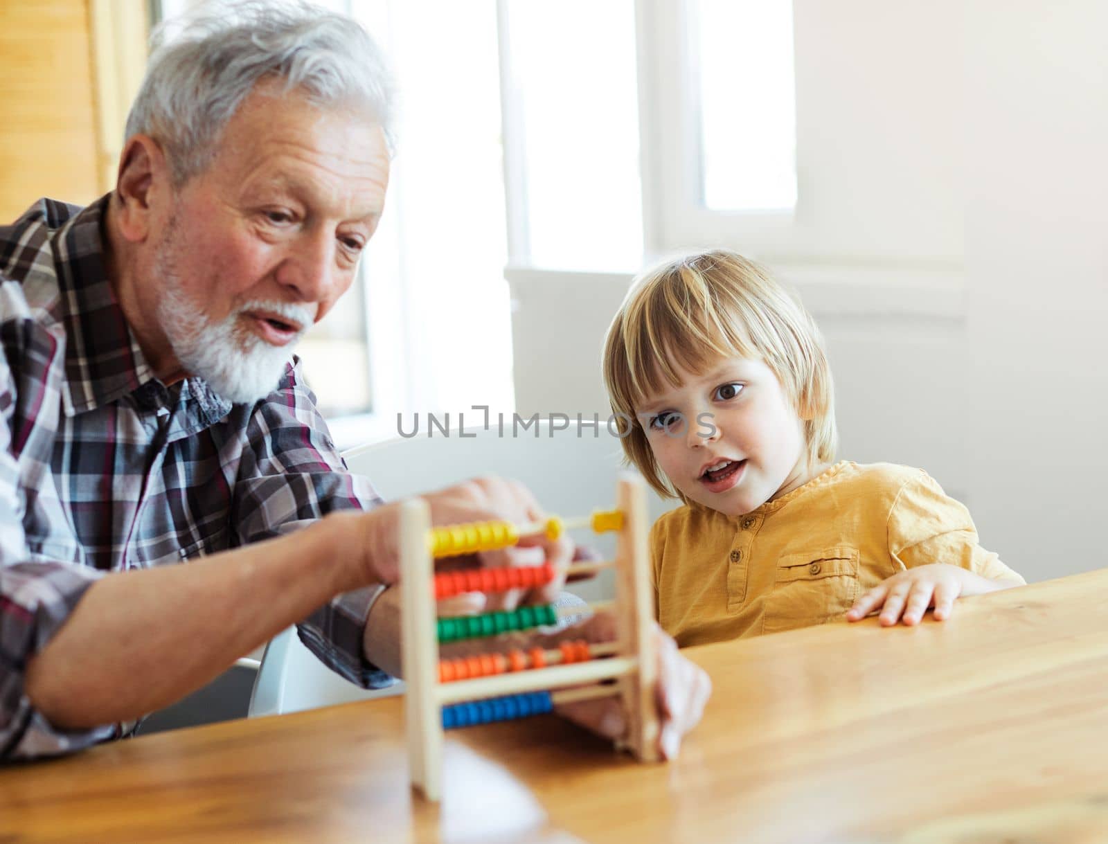 Portrait of grandfather and grandson having fun with an abacus tool or toy doing mathematic calculation and learning together at home