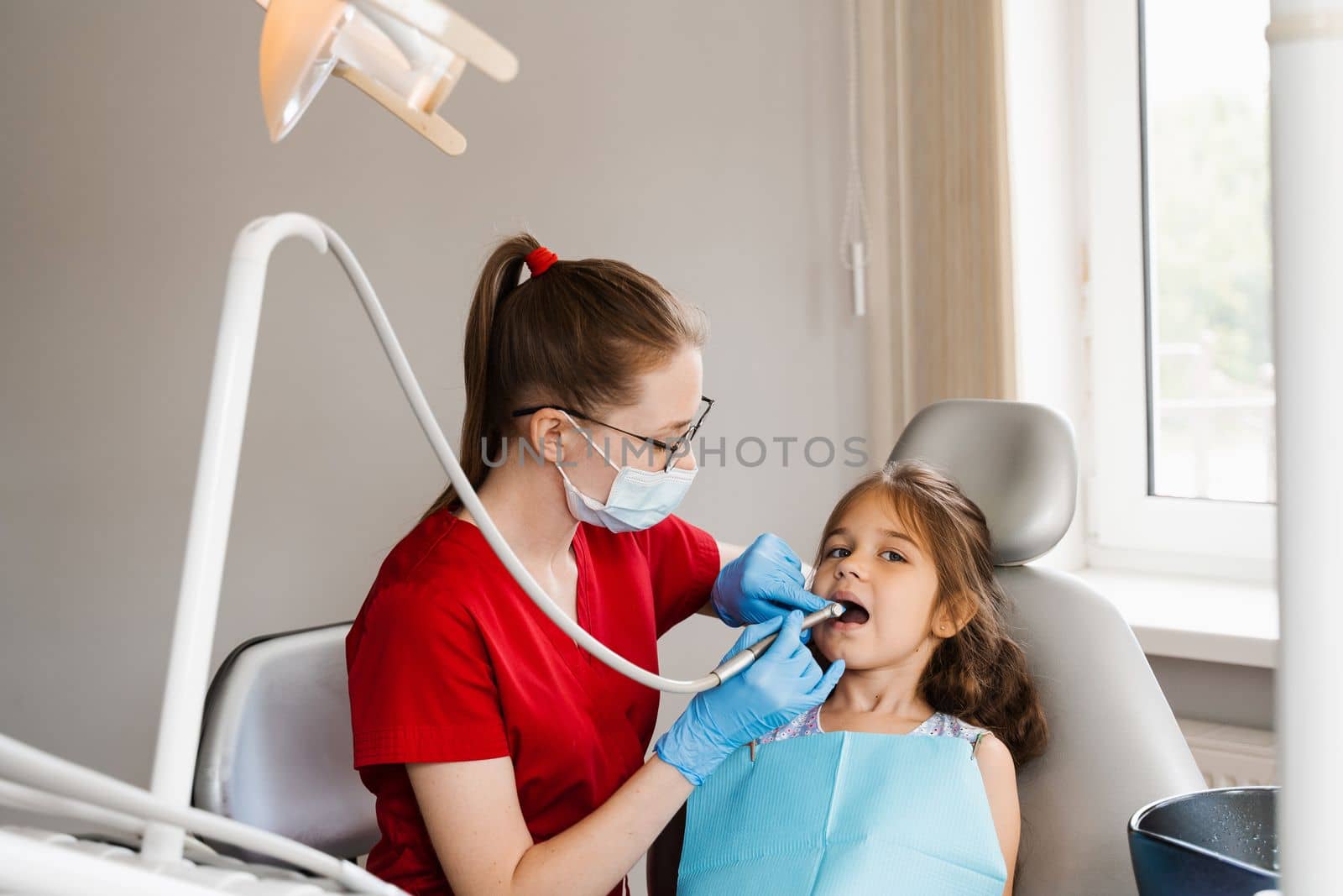 Child dentist with dental drill treats child girl in dentistry clinic. Dental filling for child patient. by Rabizo